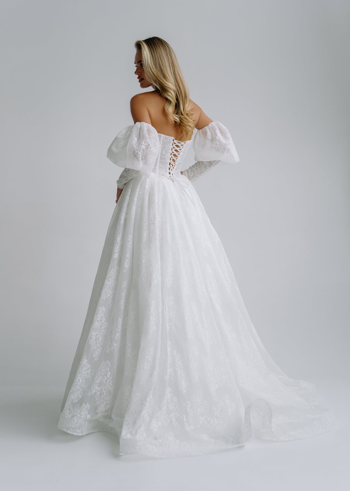 Back view of a lace wedding dress with puff sleeves, a lace-up back and a train