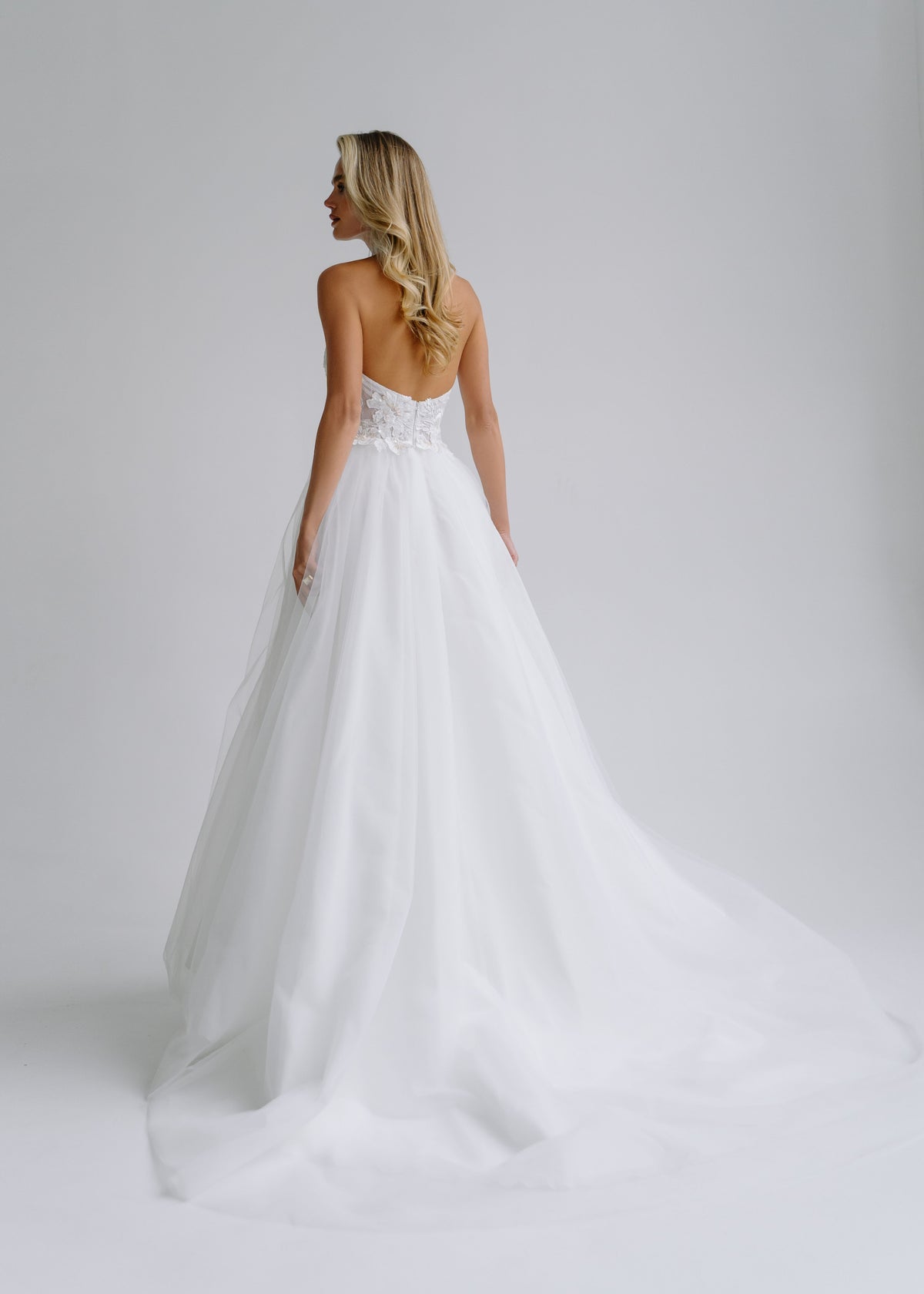 Back view of a tulle wedding dress with an open back and a flowing train