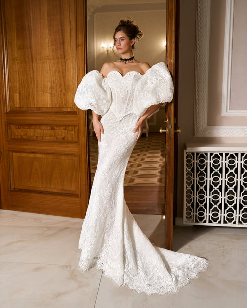 Mermaid lace wedding dress with sweetheart corset bodice and large puffy sleeves, standing in a doorway