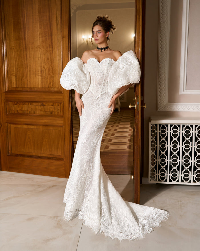 Mermaid lace wedding dress with sweetheart corset bodice and large puffy sleeves, standing in a doorway