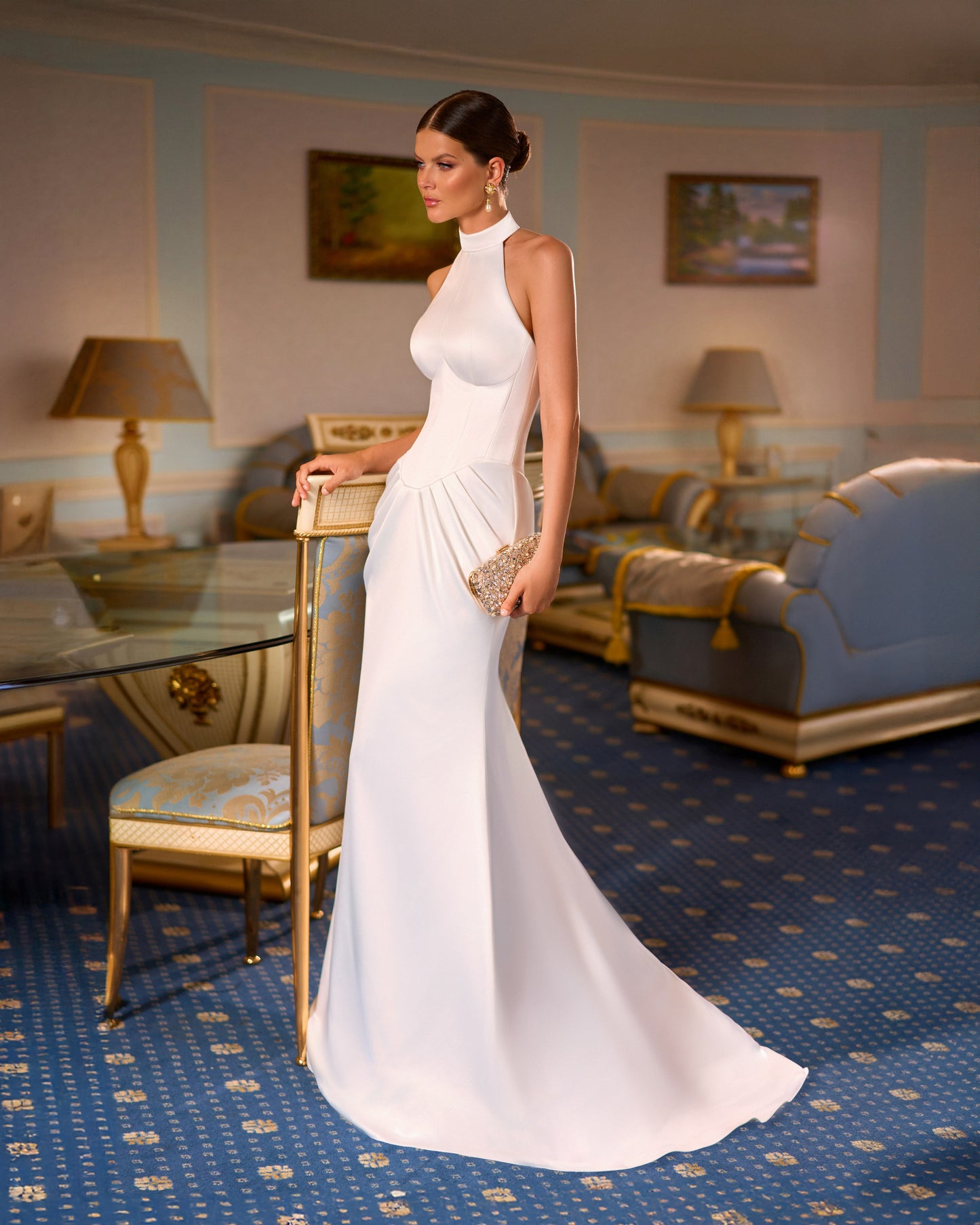 Bride wearing satin fitted sleeveless halter neck wedding dress with drop-down waist, draped hip detail, and sweep train.