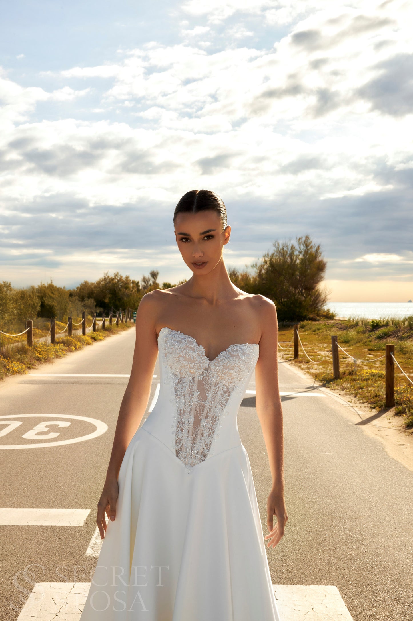 Bride in classic A-line atlas wedding gown with lace detail, V-cut neckline, drop waist, straight zip-closure back, and chapel train.