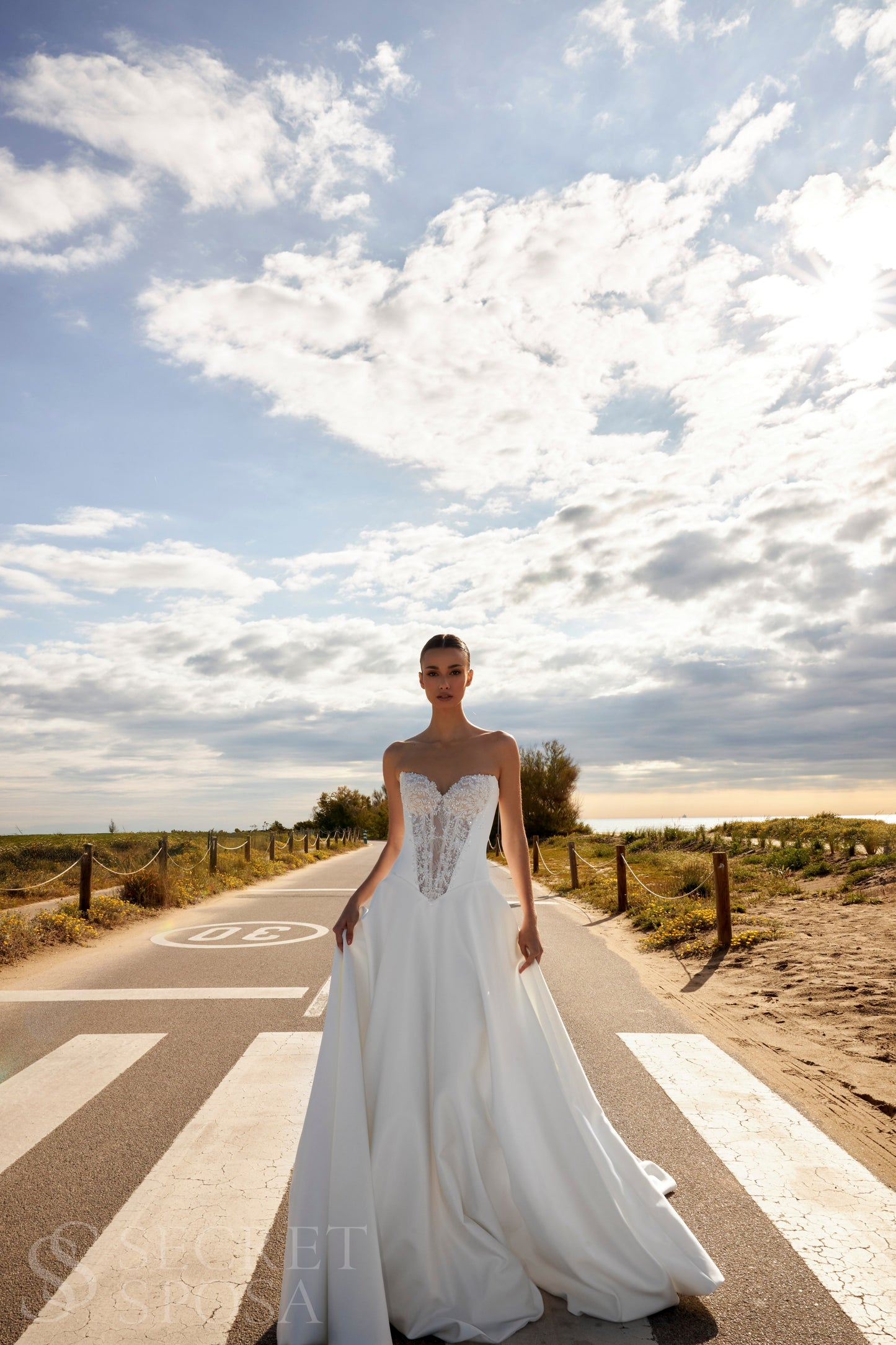 Bride in classic A-line atlas wedding gown with lace detail, V-cut neckline, drop waist, straight zip-closure back, and chapel train.