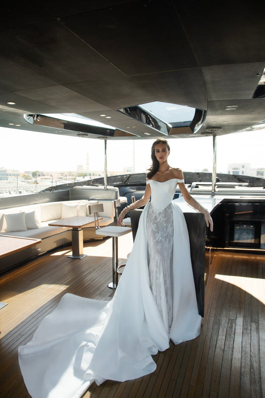 Bride wearing an off-shoulder corset wedding gown with train and optional Mikado overskirt from the Celeste Collection, photographed on a yacht.