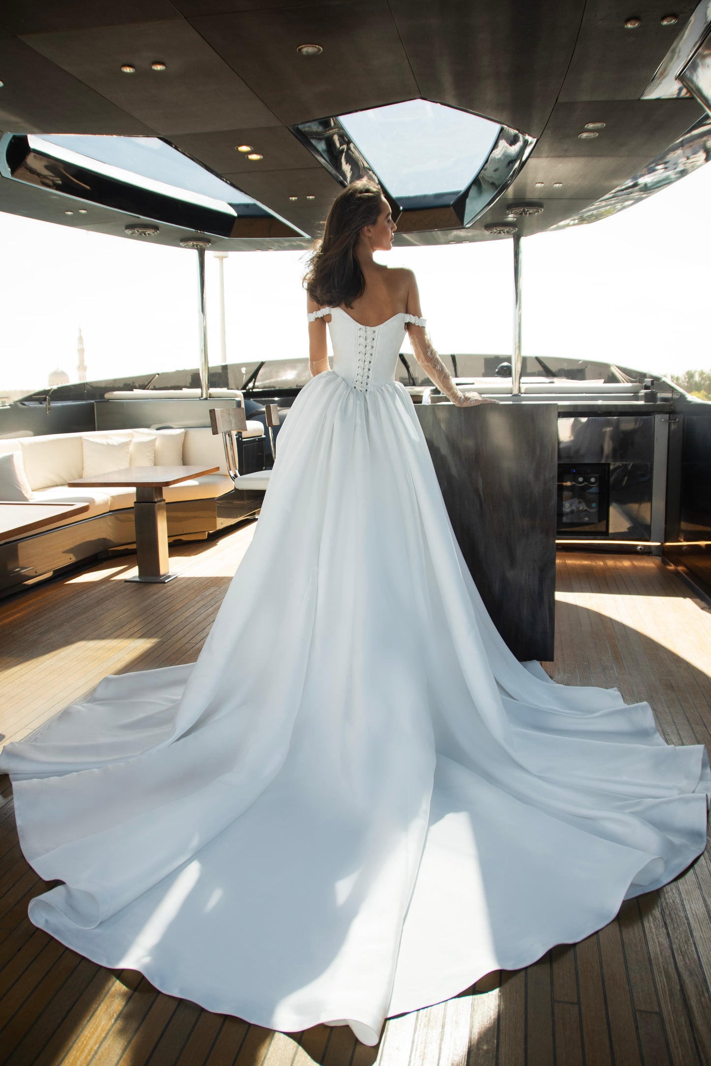 Bride wearing an off-shoulder corset wedding gown with train and optional Mikado overskirt from the Celeste Collection, photographed on a yacht.