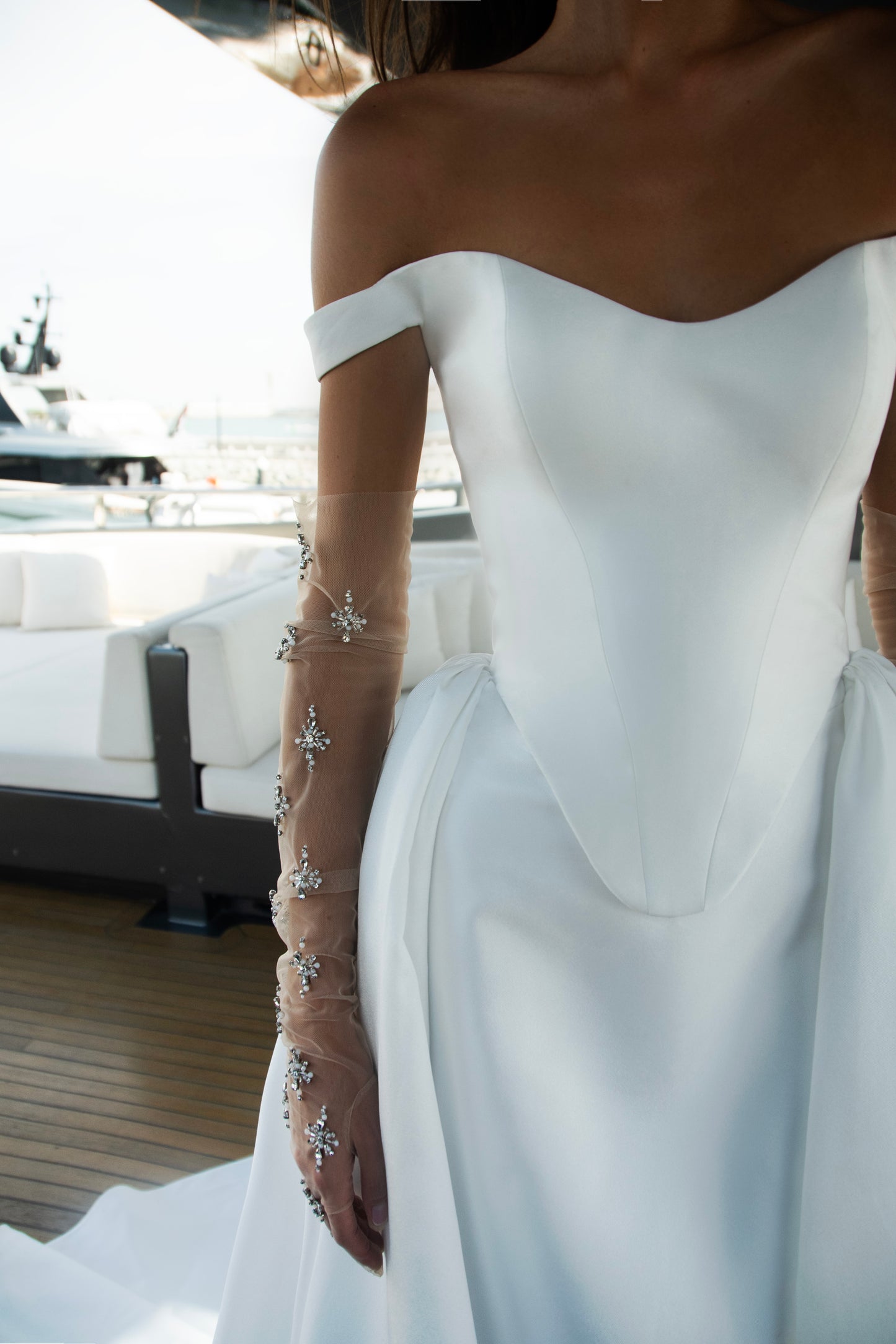Bride wearing an off-shoulder corset wedding gown with train and optional Mikado overskirt from the Celeste Collection, photographed on a yacht.