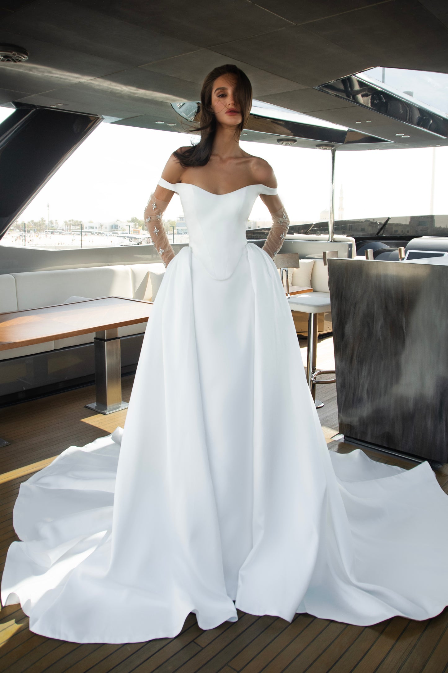 Bride wearing an off-shoulder corset wedding gown with train and optional Mikado overskirt from the Celeste Collection, photographed on a yacht.