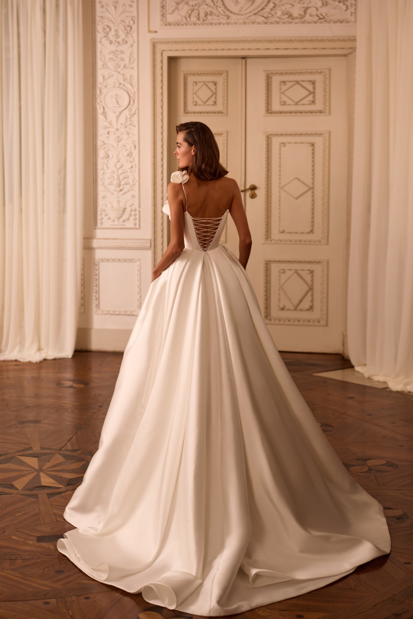 Bride in Mikado A-line wedding dress with one-shoulder floral strap, high slit, and lace-up back, standing confidently in soft natural light.