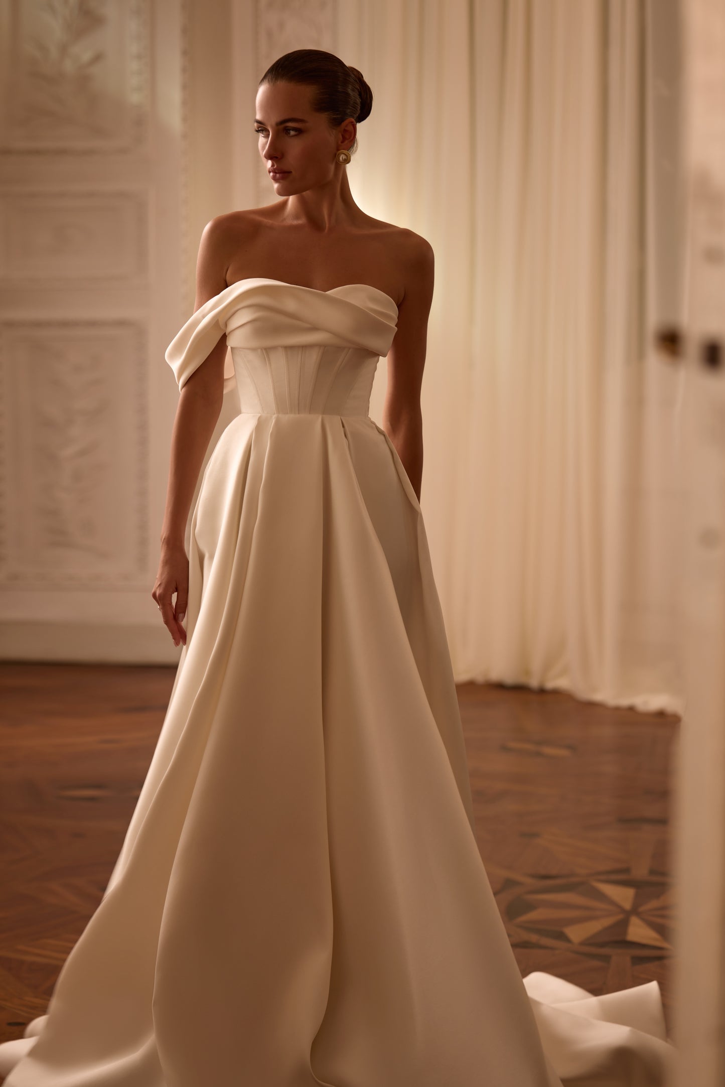 Bride in sleeveless A-line Mikado wedding gown with draped one-shoulder neckline, thigh-high slit, lace-up back, and court train in soft light.