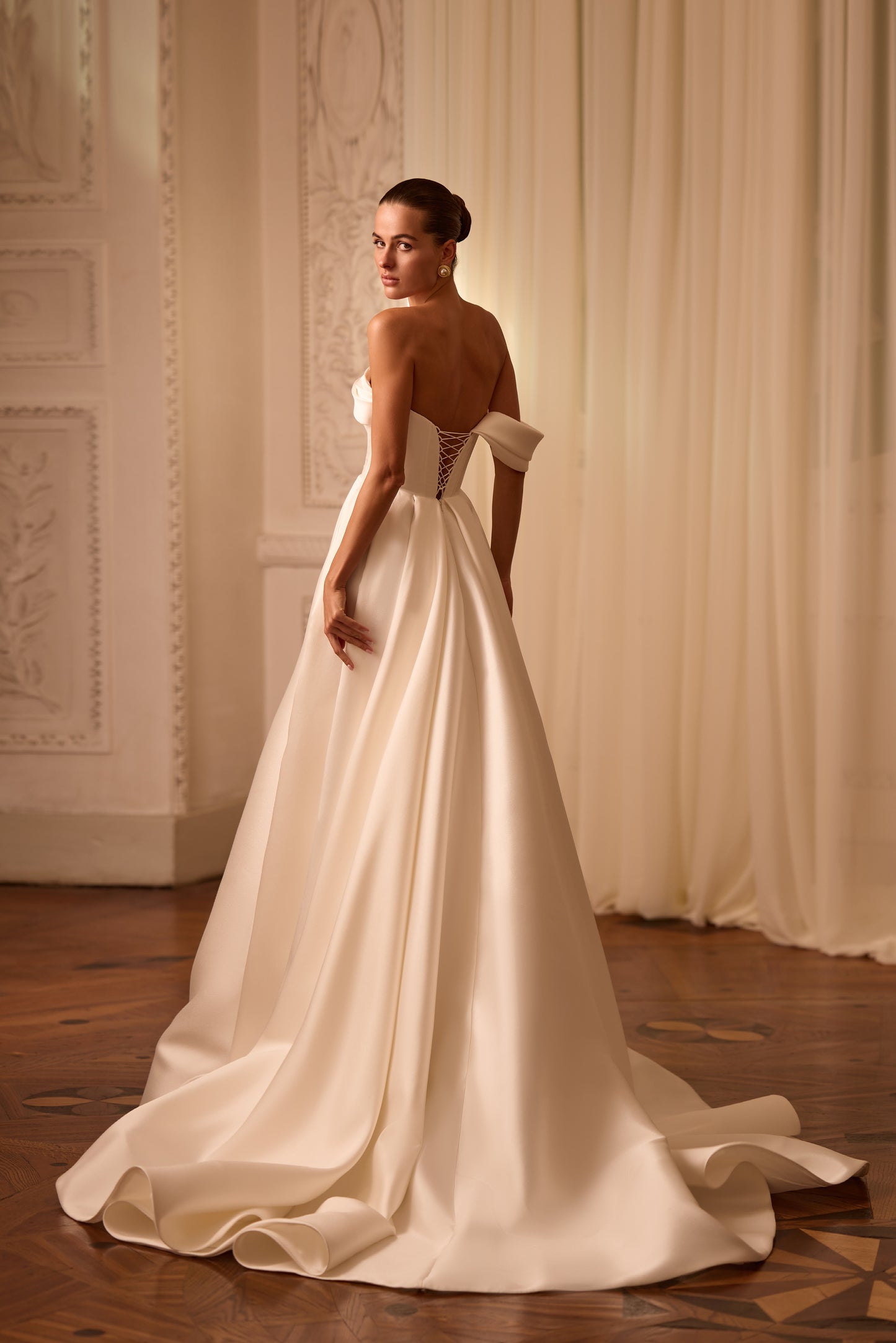 Bride in sleeveless A-line Mikado wedding gown with draped one-shoulder neckline, thigh-high slit, lace-up back, and court train in soft light.
