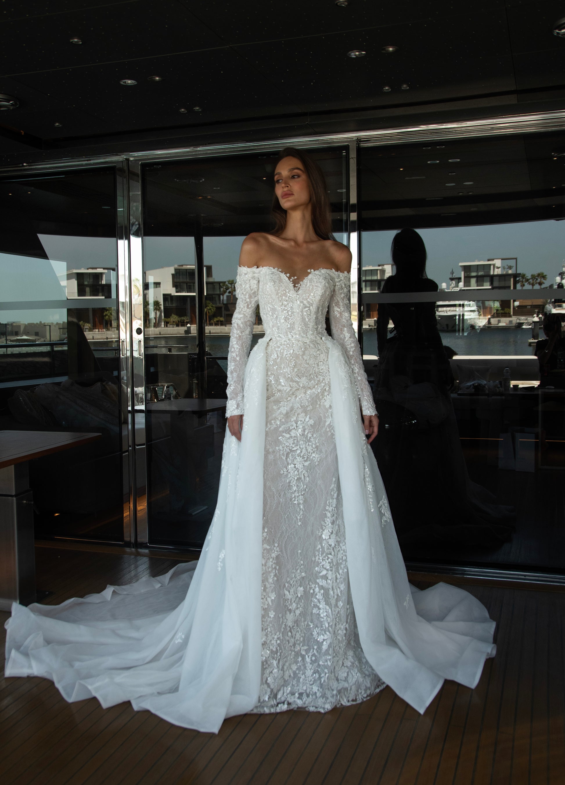 Camber off-shoulder lace wedding gown with detachable tulle overskirt. A romantic mermaid silhouette with illusion sleeves, hand-applied lace, and a sculpted corset bodice for two stunning bridal looks in one.