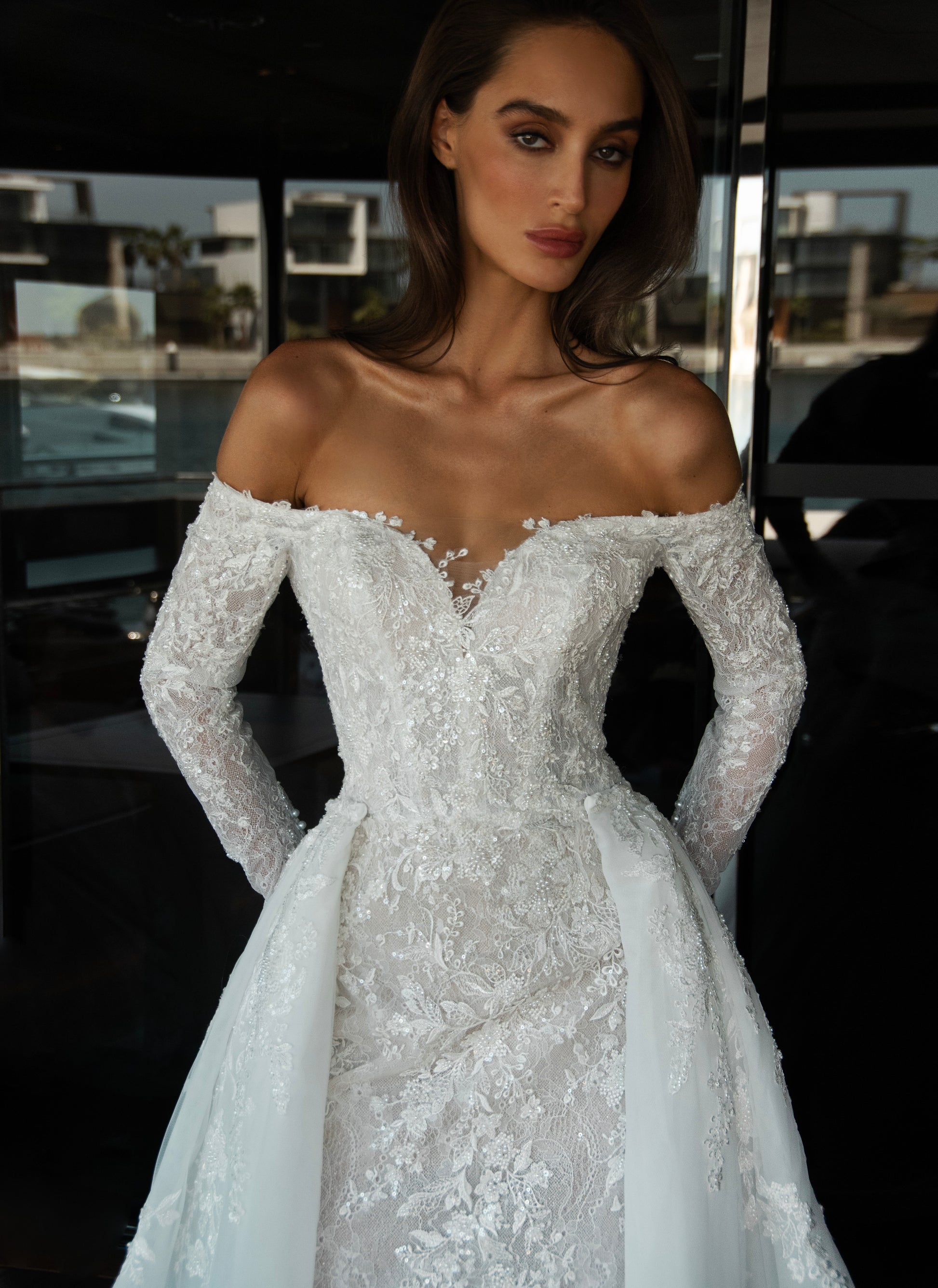 Camber off-shoulder lace wedding gown with detachable tulle overskirt. A romantic mermaid silhouette with illusion sleeves, hand-applied lace, and a sculpted corset bodice for two stunning bridal looks in one.