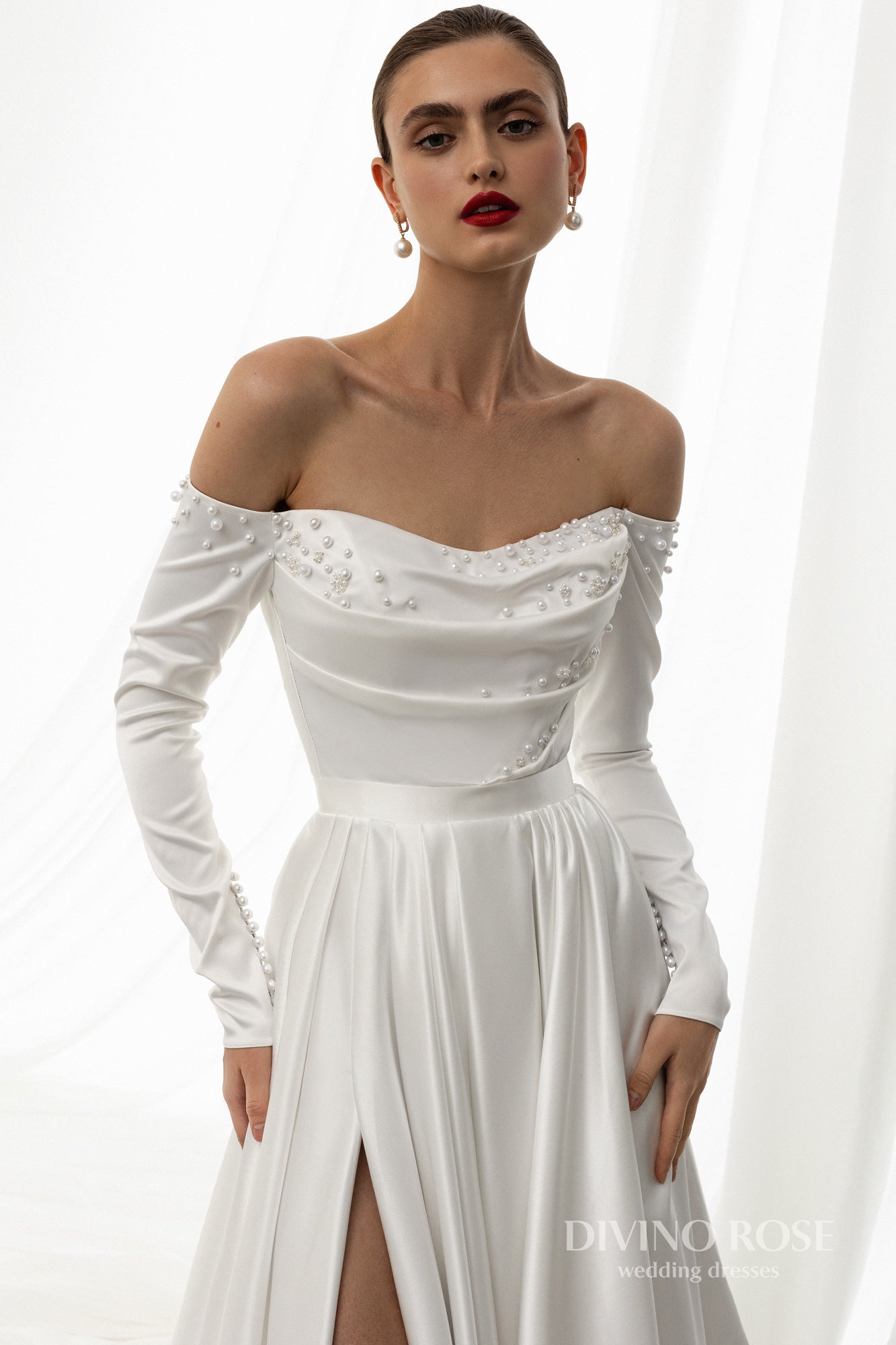 Off-shoulder satin wedding dress with long sleeves and slit.