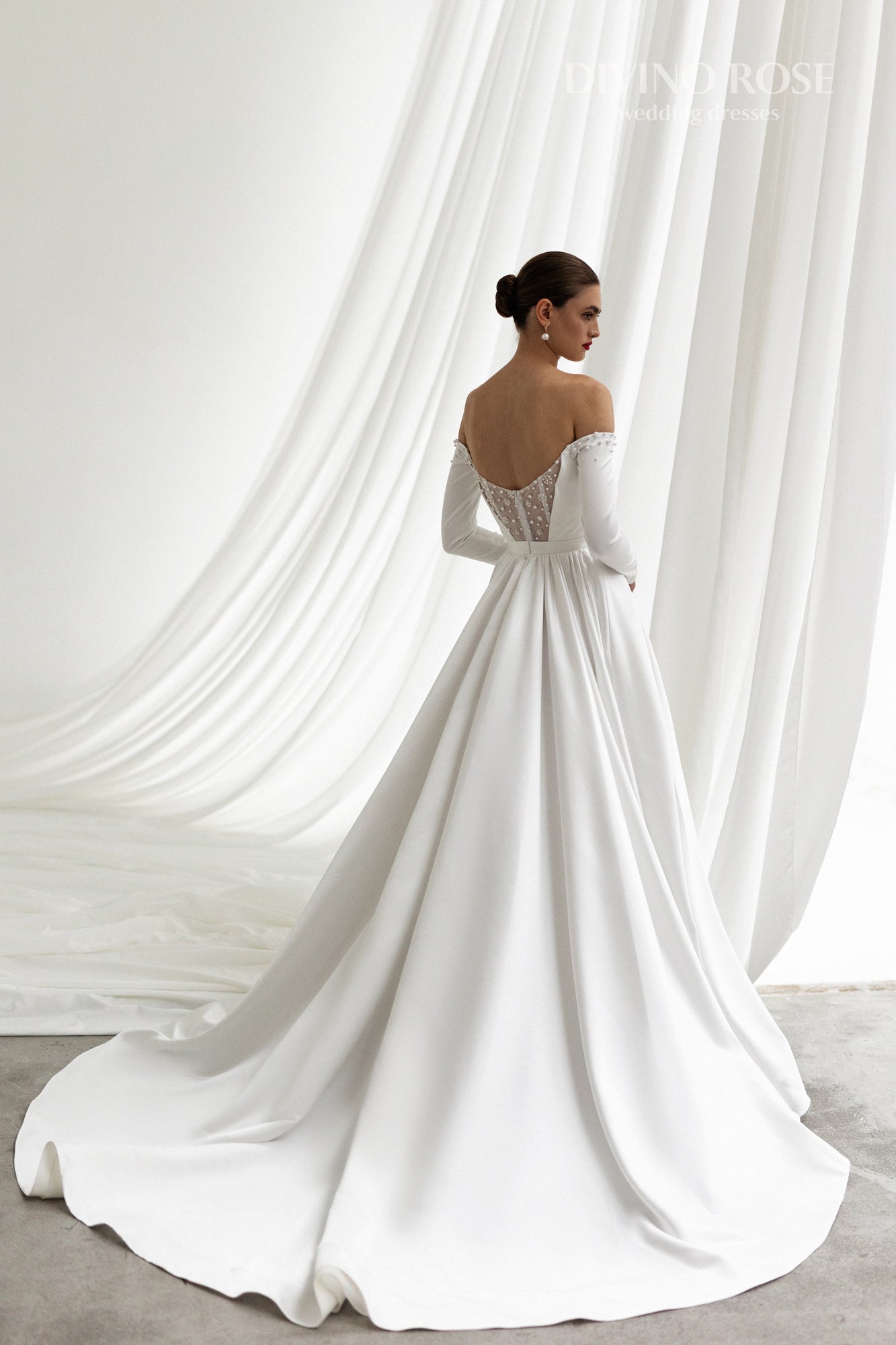 Off-shoulder satin wedding dress with long sleeves and slit.