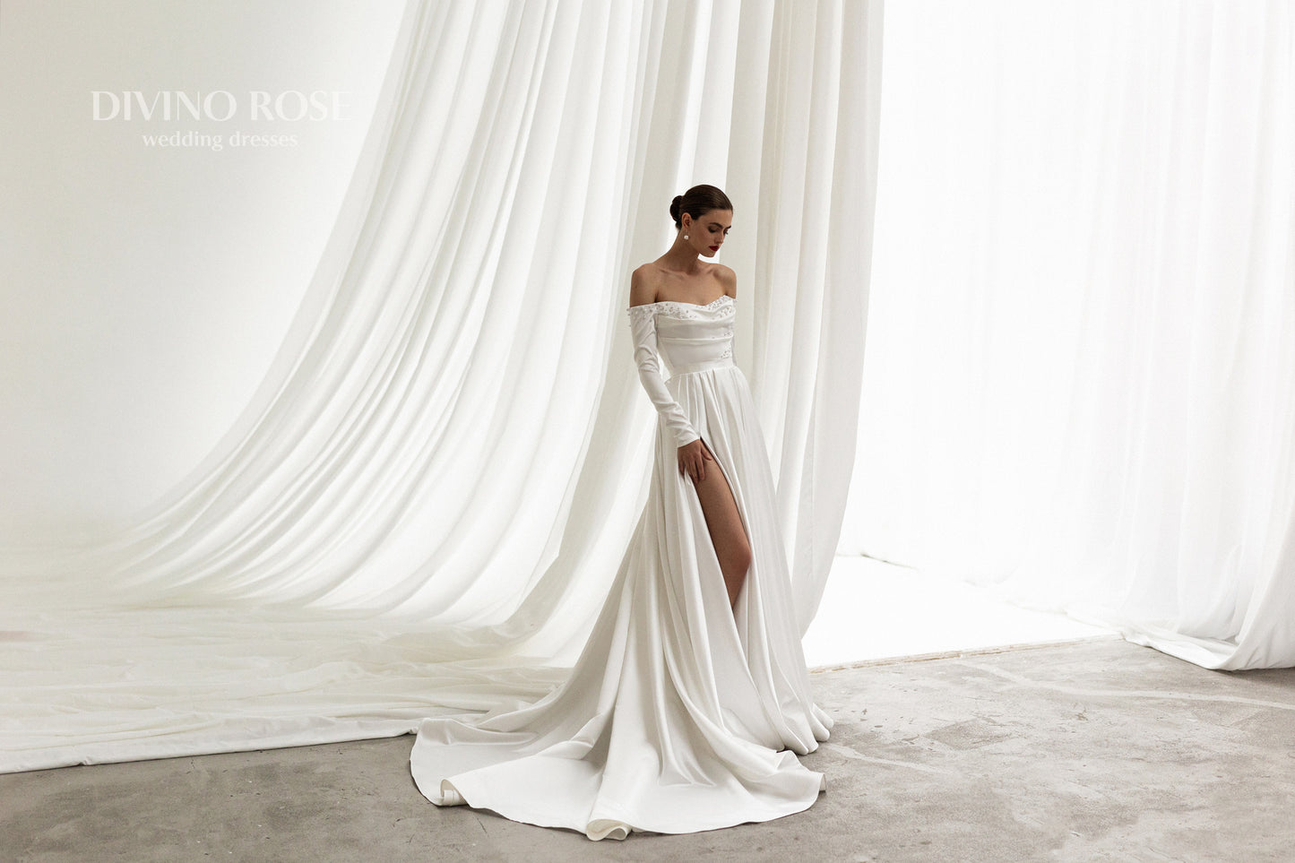Off-shoulder satin wedding dress with long sleeves and slit.