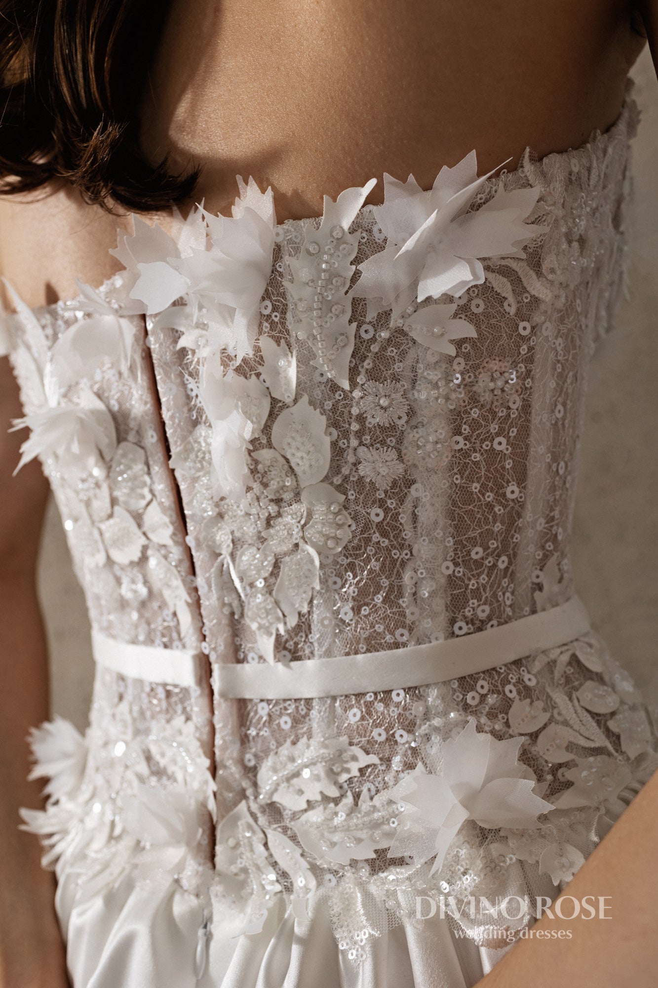 Sleeveless wedding dress with lace corset and floral details.
