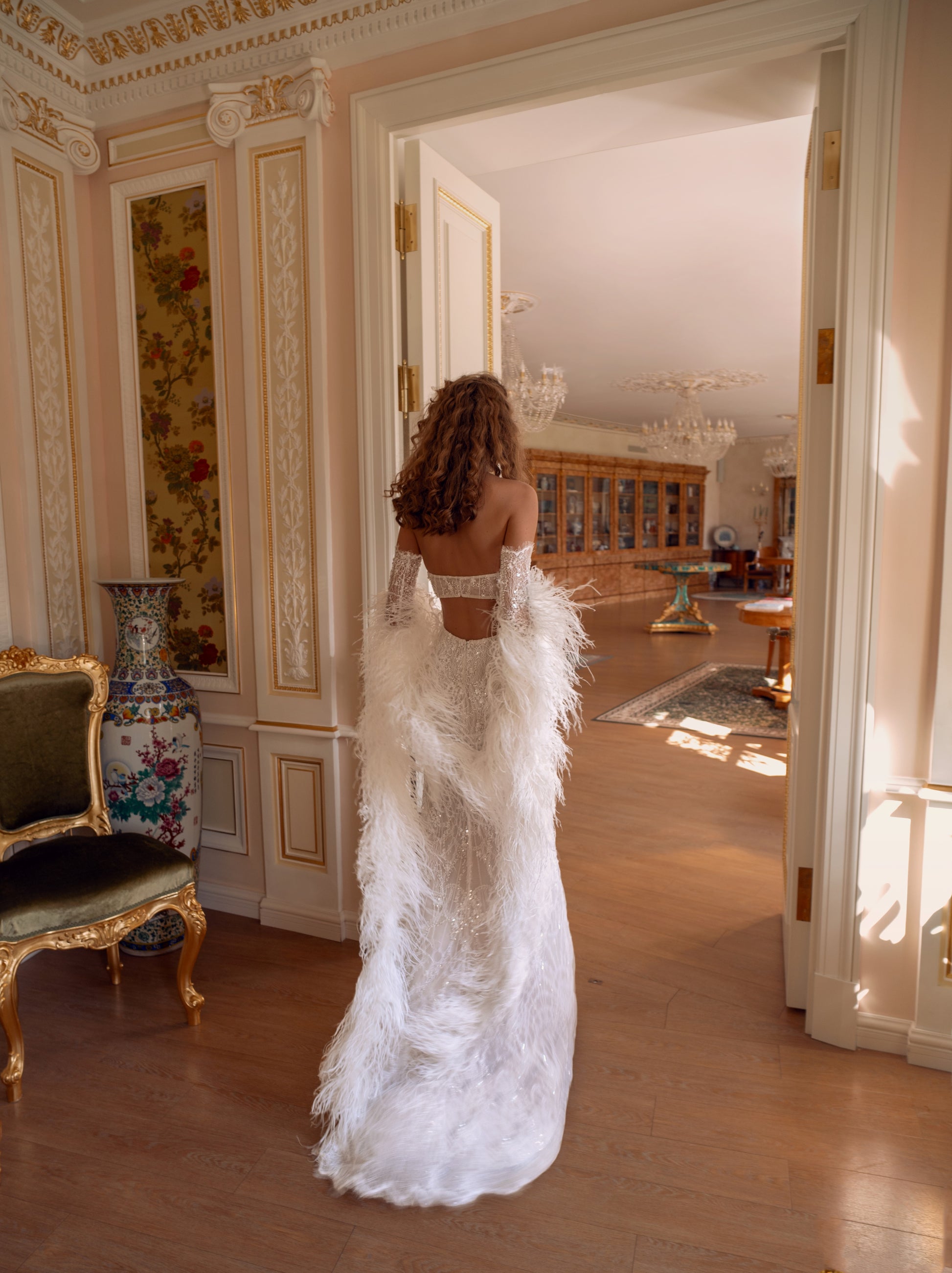 An elegant halter column wedding gown crafted in hand-beaded lace with detachable lace sleeves and a dramatic feather stole. Modern, sculpted, and exquisitely glamorous.