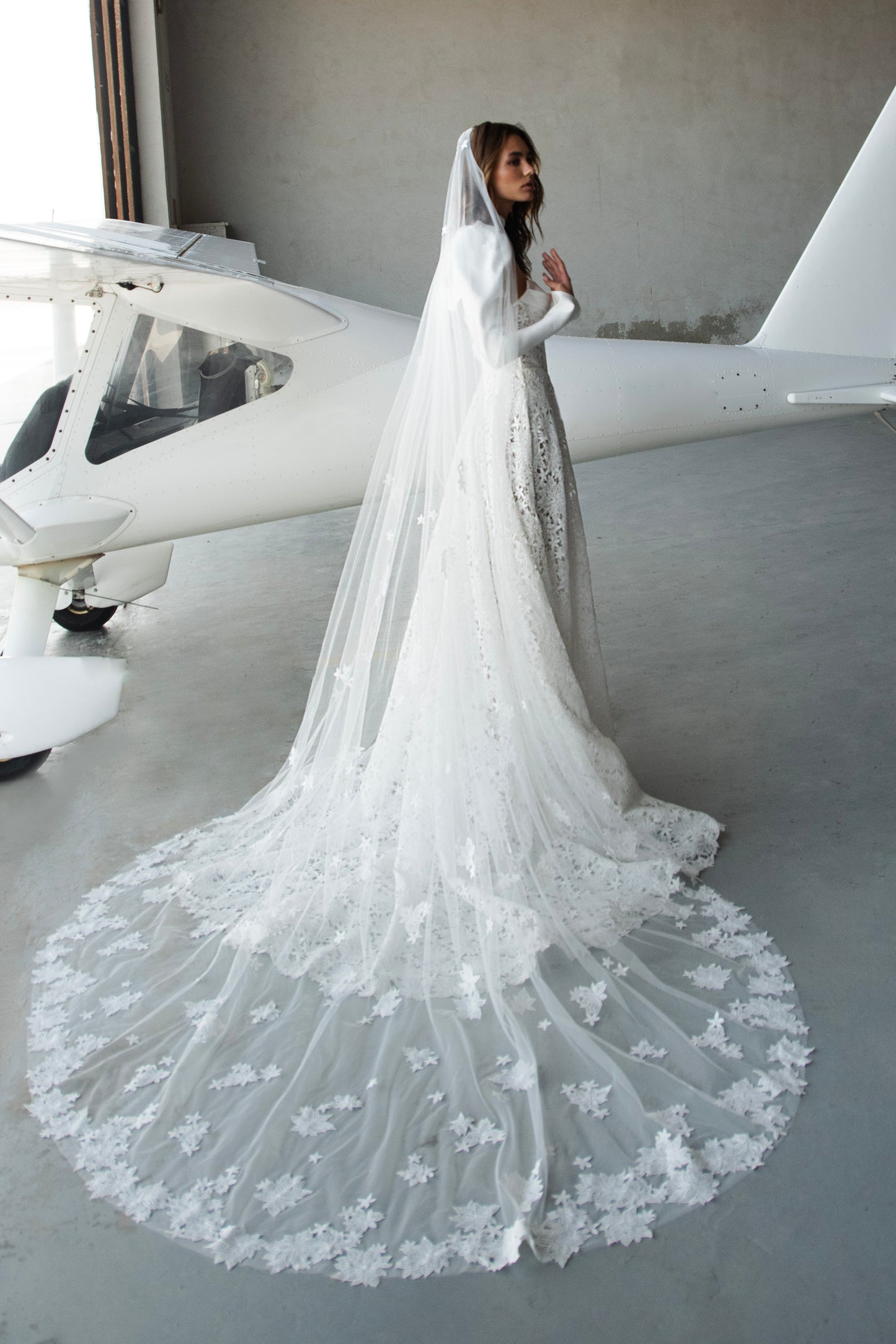 Bride in lace A-line wedding dress with satin bolero, sweetheart corset bodice, long sleeves, and chapel train.