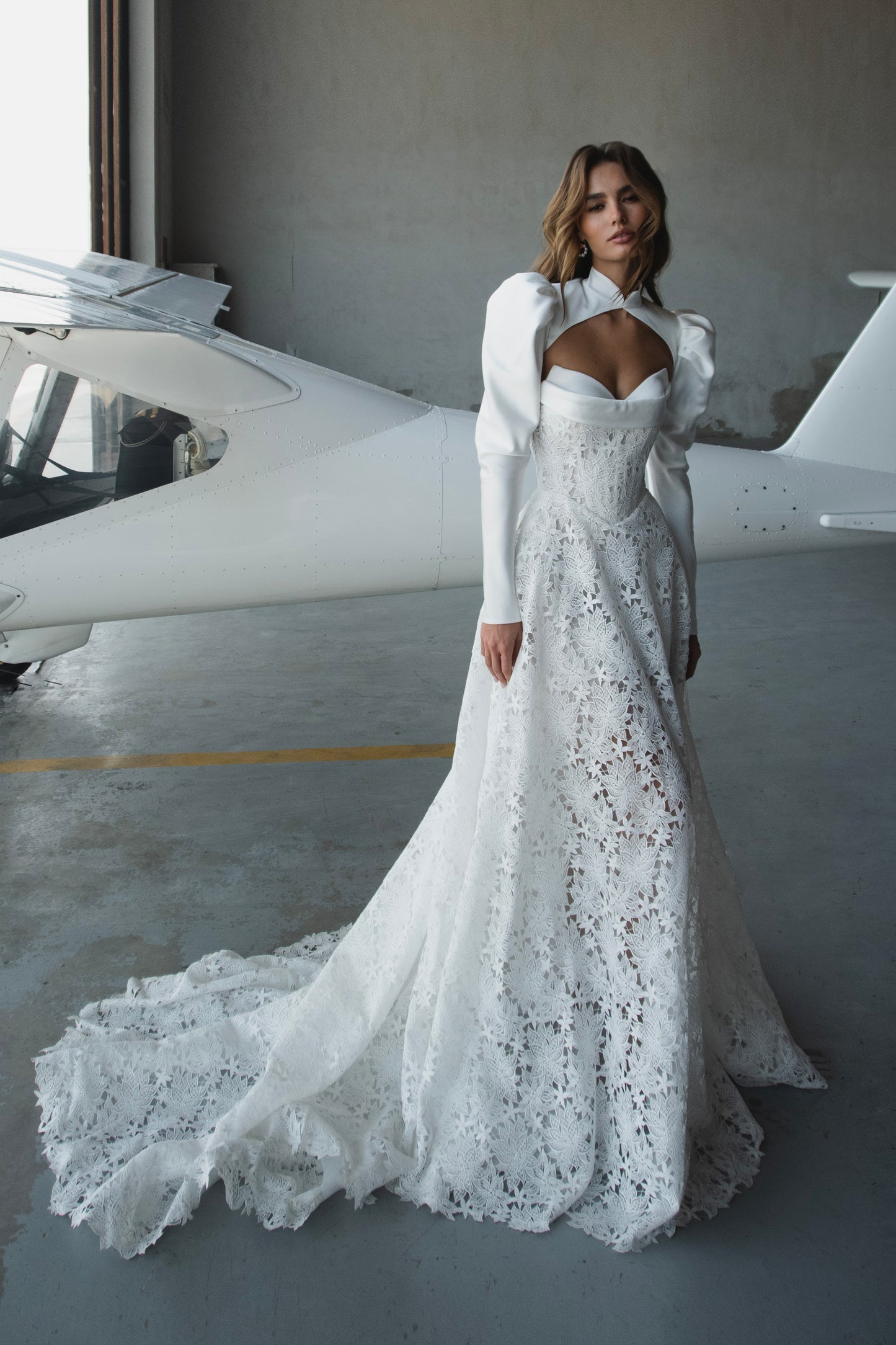 Bride in lace A-line wedding dress with satin bolero, sweetheart corset bodice, long sleeves, and chapel train.