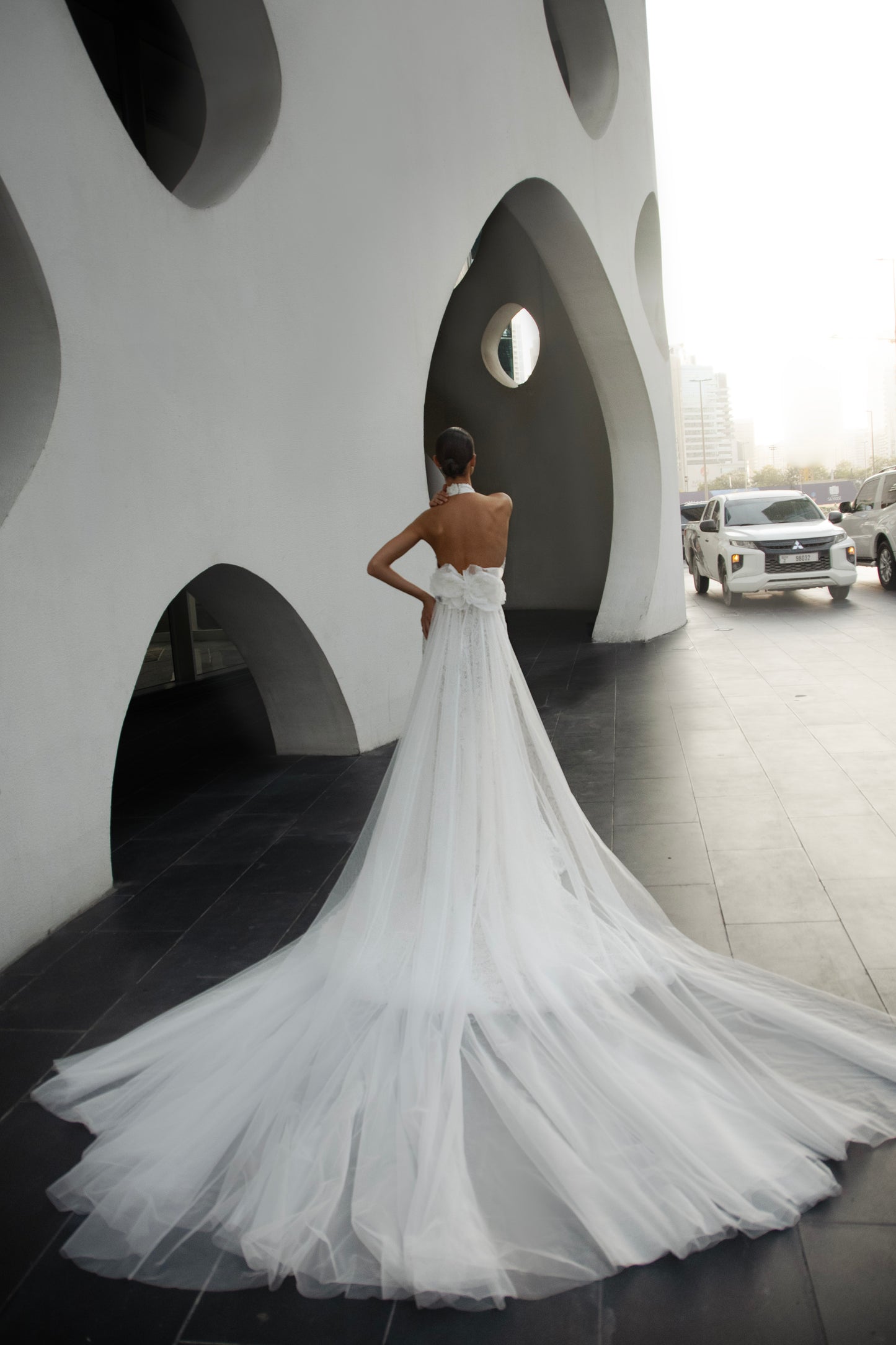 Backless halter lace sheath wedding dress with detachable tulle overskirt and cathedral train, photographed in the city.