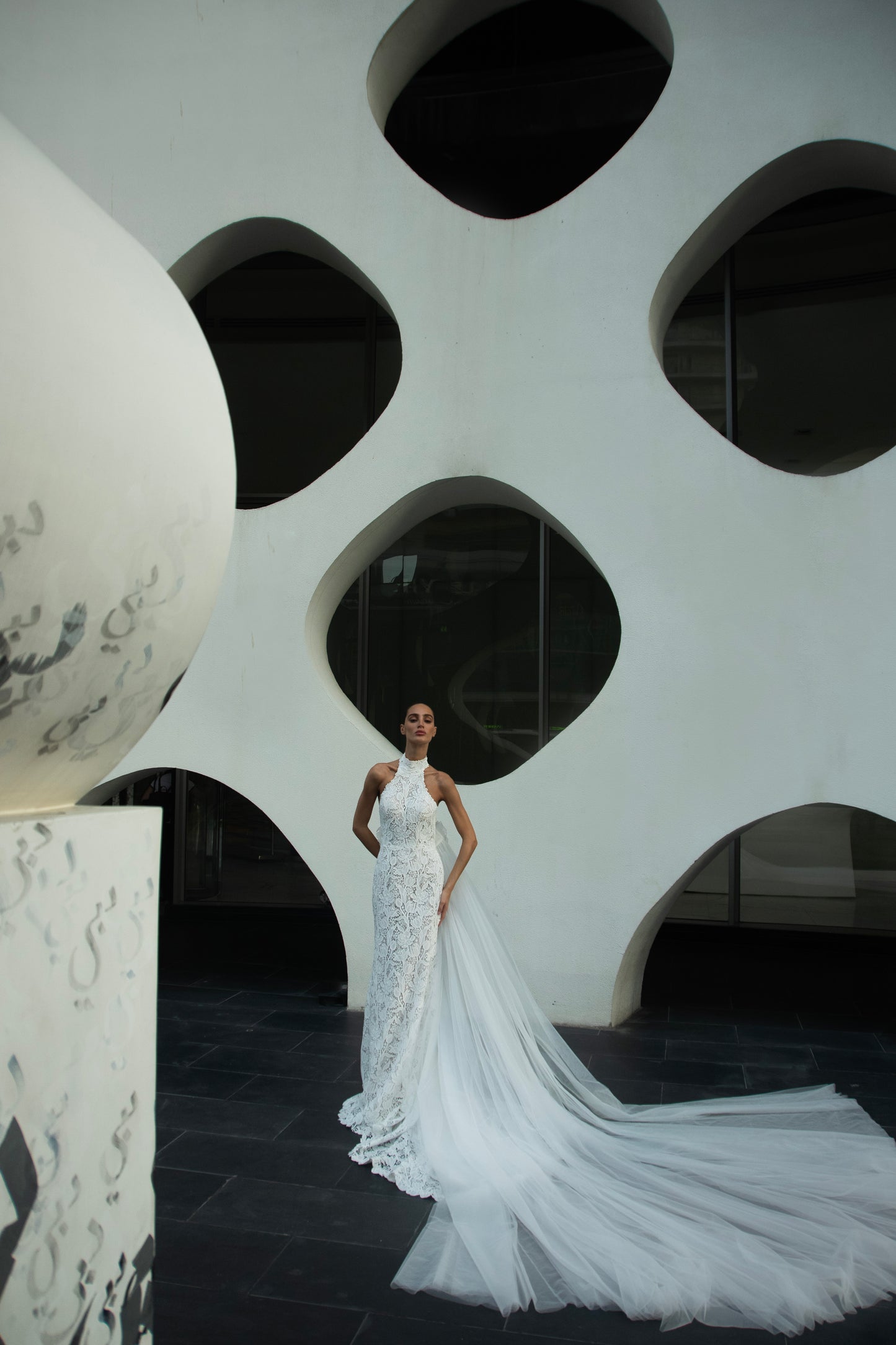 Backless halter lace sheath wedding dress with detachable tulle overskirt and cathedral train, photographed in the city.