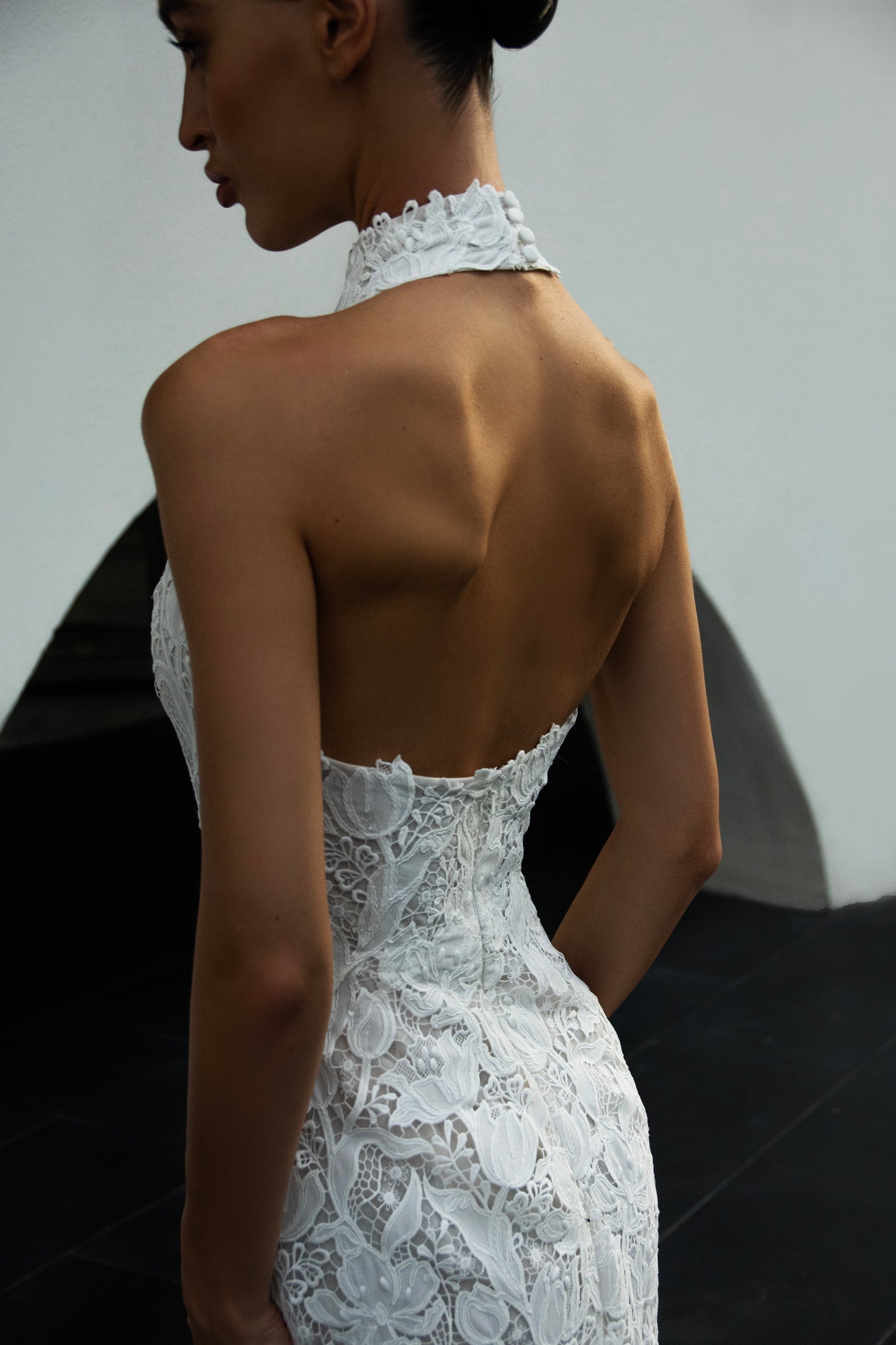 Backless halter lace sheath wedding dress with detachable tulle overskirt and cathedral train, photographed in the city.
