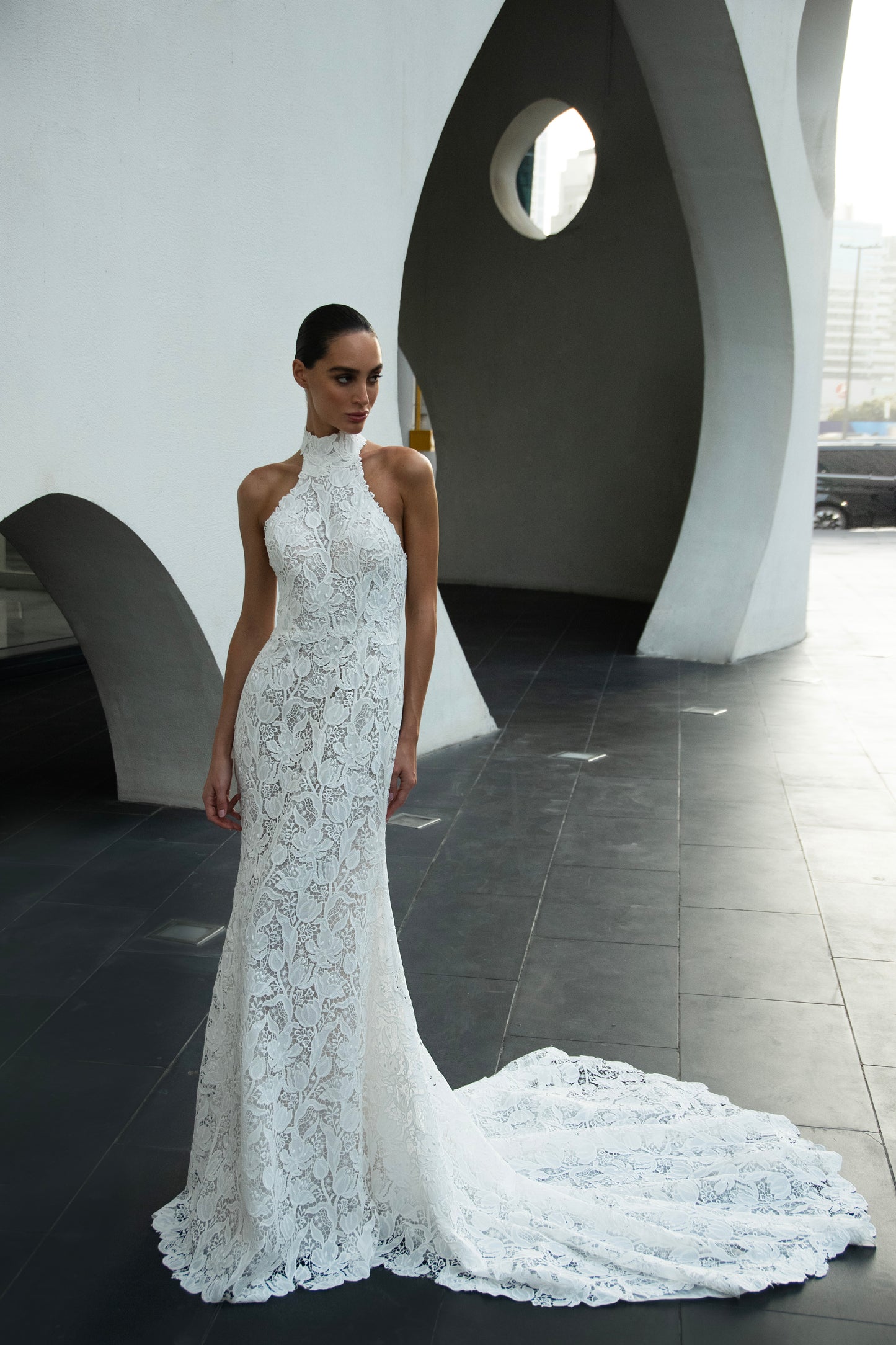 Backless halter lace sheath wedding dress with detachable tulle overskirt and cathedral train, photographed in the city.