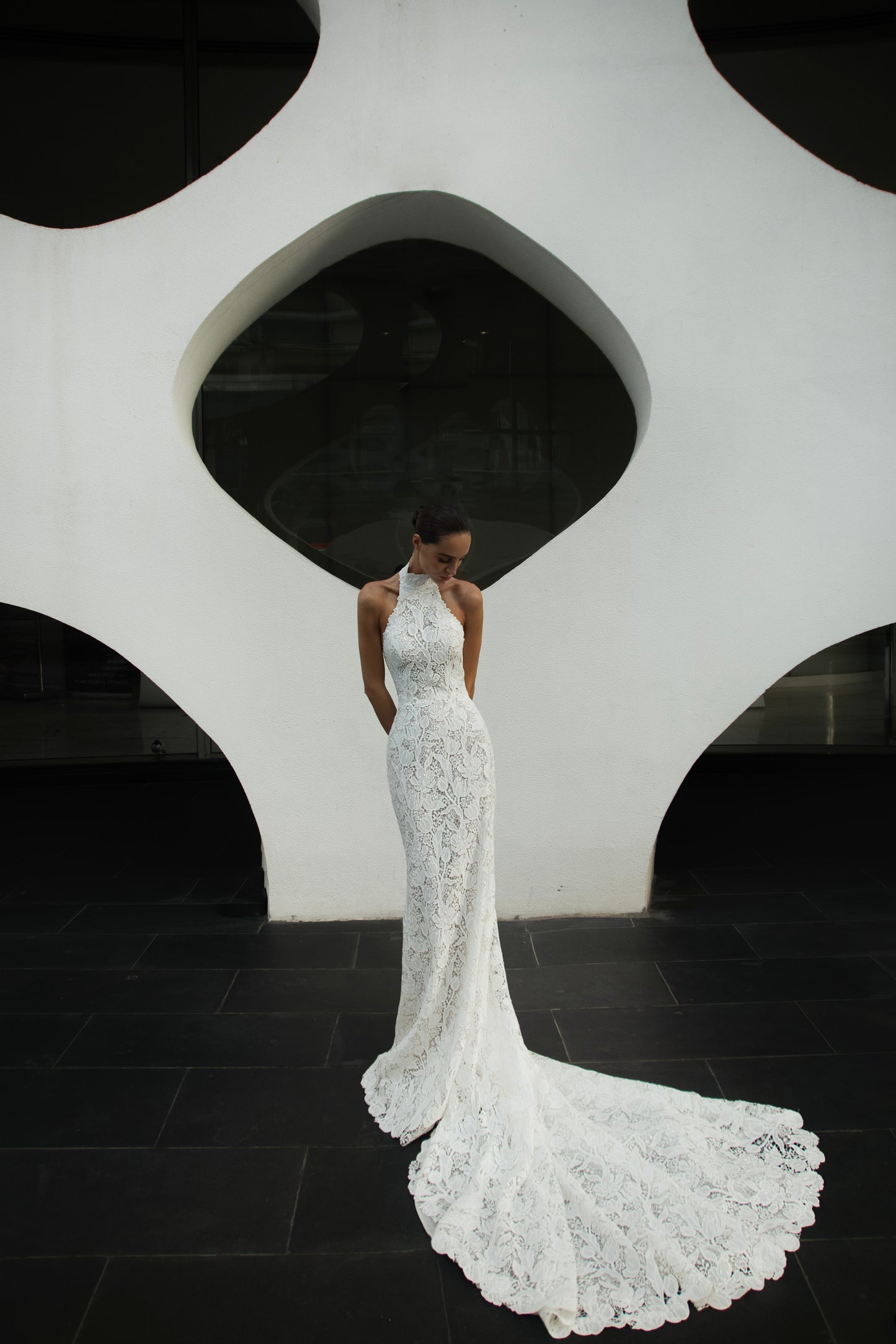 Backless halter lace sheath wedding dress with detachable tulle overskirt and cathedral train, photographed in the city.