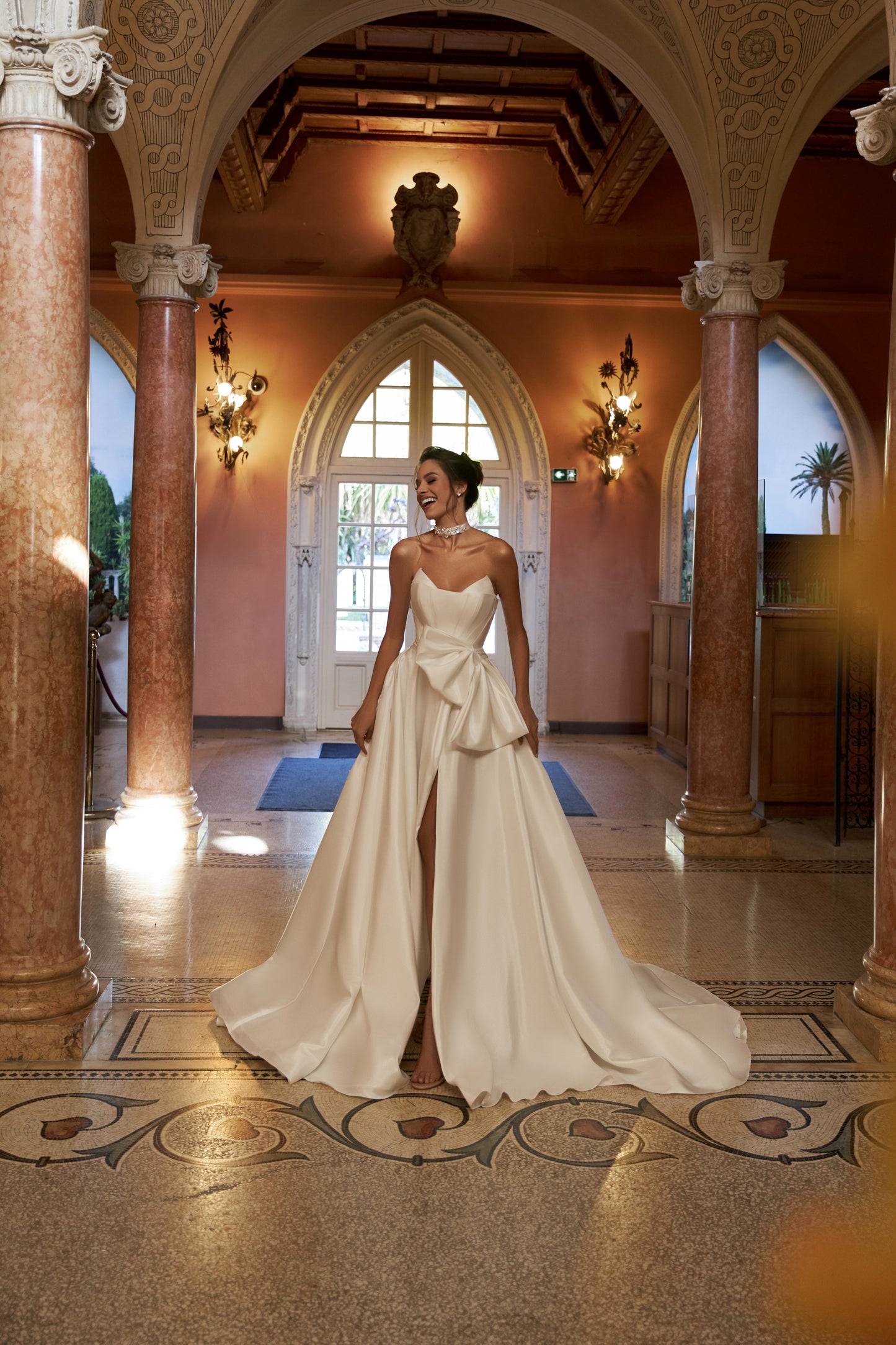 A-line wedding dress with a sleeveless bodice, open back, and pleated slit skirt. Features a zircon-embroidered belt with a bow, detachable bow, and 50 cm train. Made of plain taffeta mikado