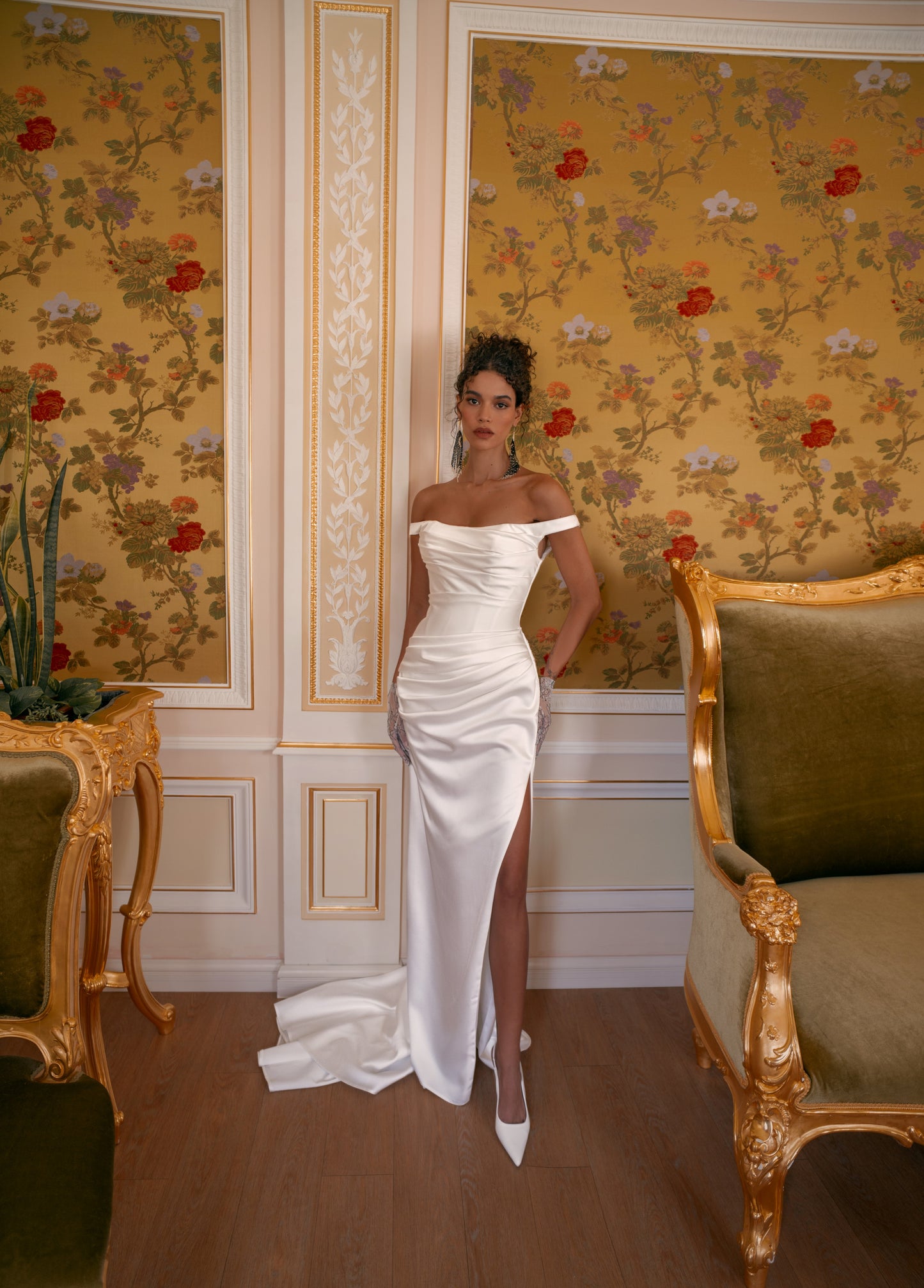 Bride in off-shoulder satin mermaid wedding gown with draped bodice, thigh-high slit, lace-up back, and sweep train.
