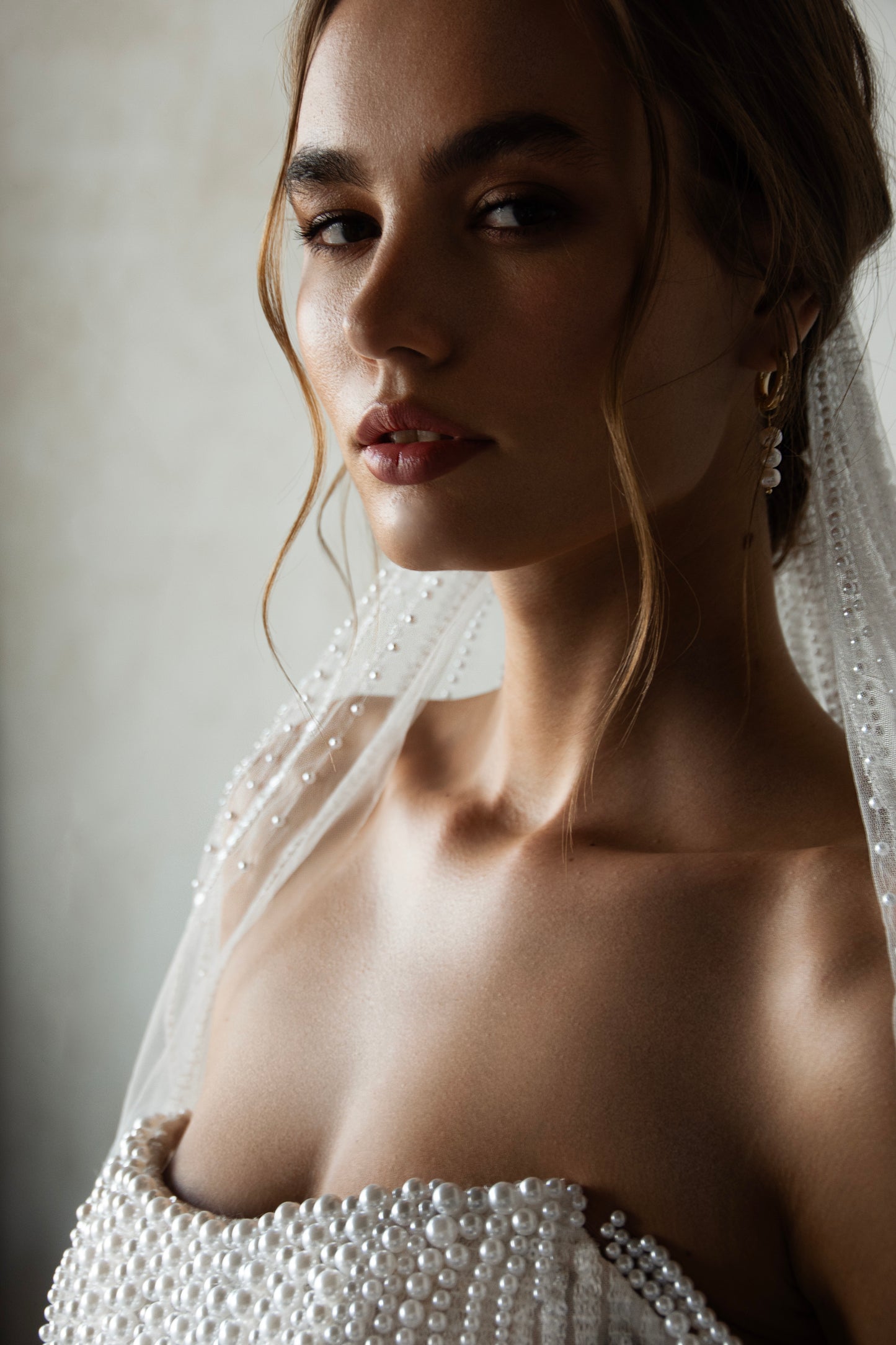 Pearl-embroidered tulle wedding dress with beaded corset bodice, detachable sheer sleeves, thigh-high slit, and flowing layered skirt