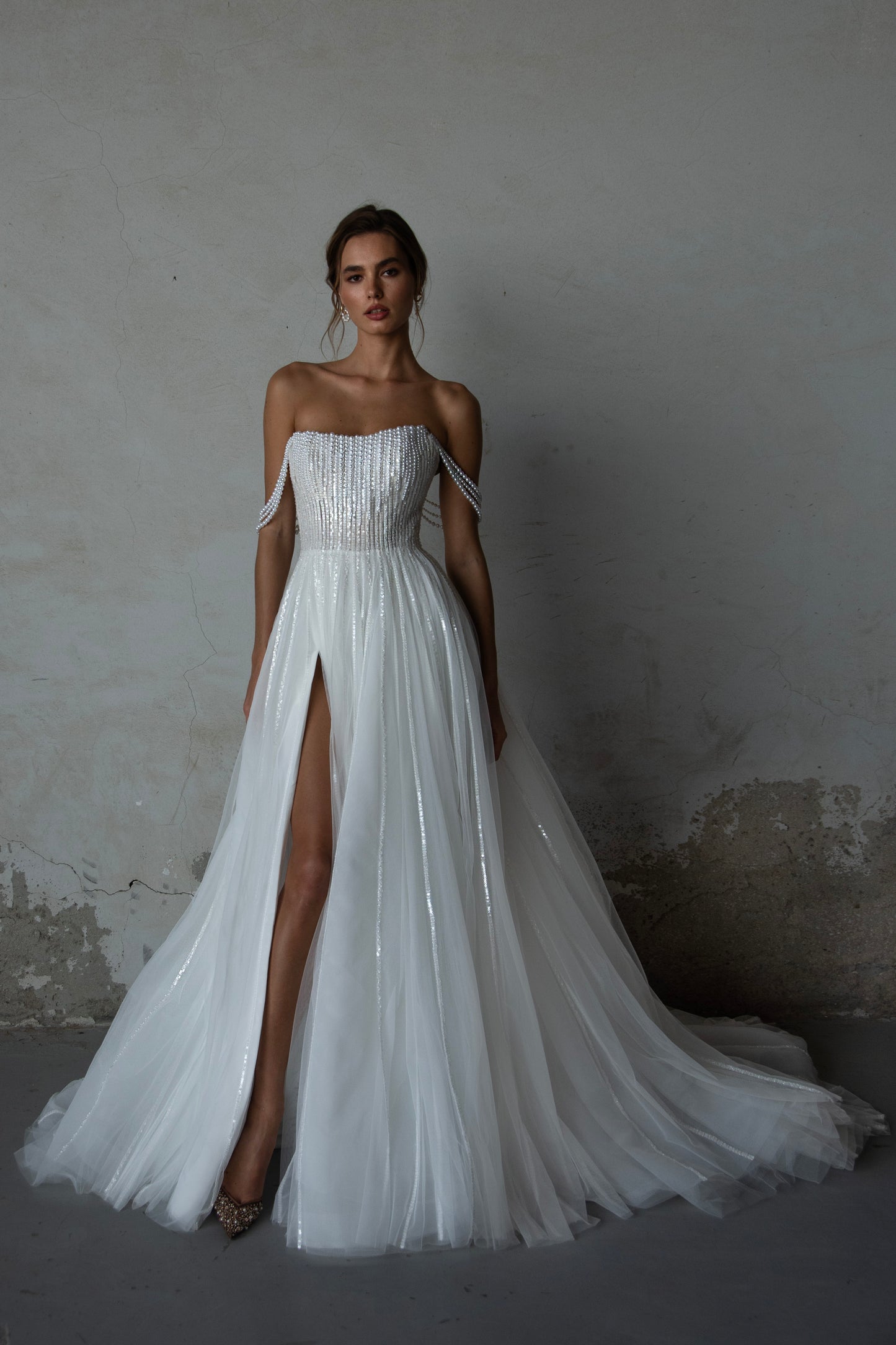 Pearl-embroidered tulle wedding dress with beaded corset bodice, detachable sheer sleeves, thigh-high slit, and flowing layered skirt