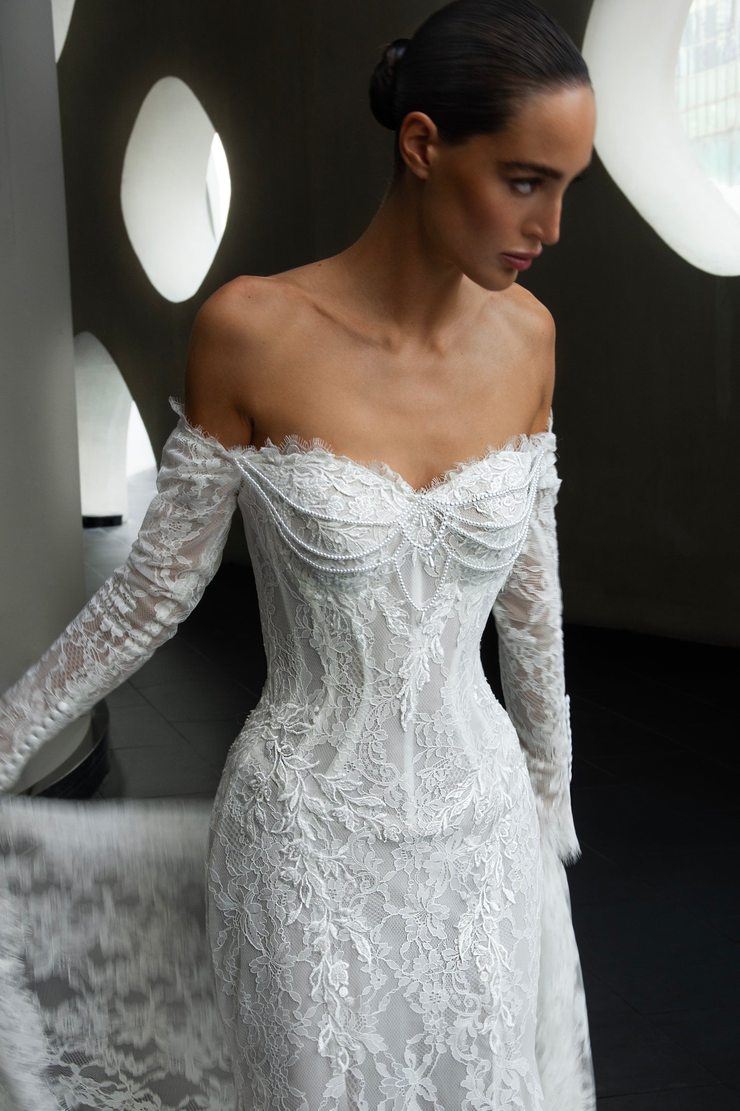 Off-shoulder lace wedding gown with long illusion sleeves, corset bodice, and chapel-length train.