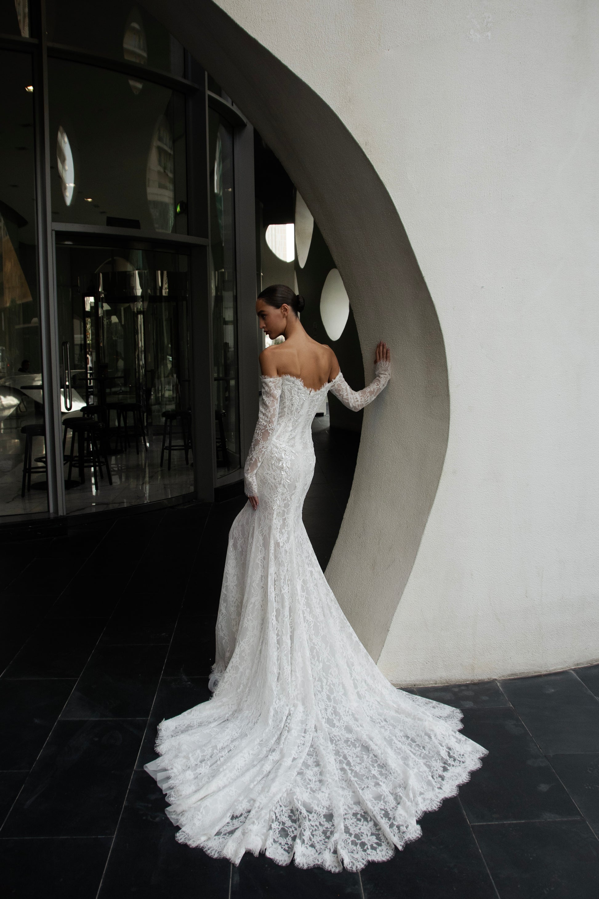 Off-shoulder lace wedding gown with long illusion sleeves, corset bodice, and chapel-length train.