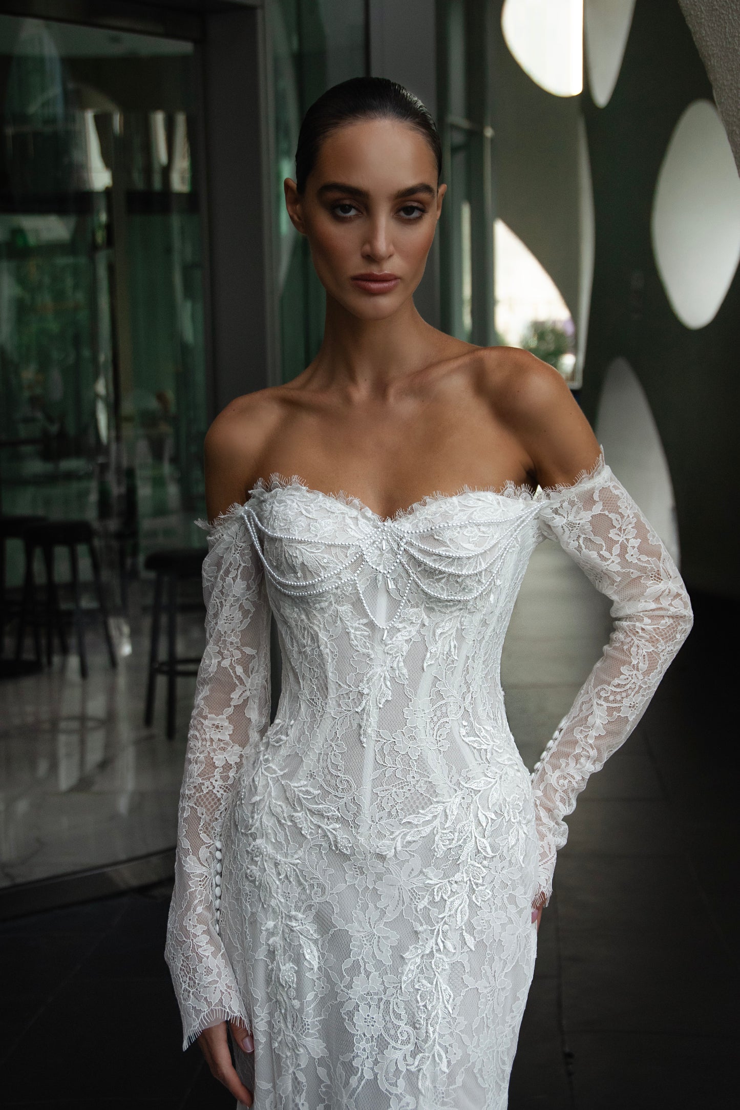 Off-shoulder lace wedding gown with long illusion sleeves, corset bodice, and chapel-length train.
