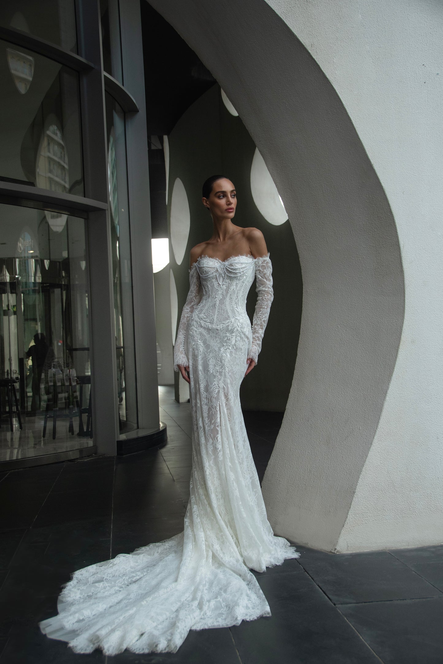 Off-shoulder lace wedding gown with long illusion sleeves, corset bodice, and chapel-length train.
