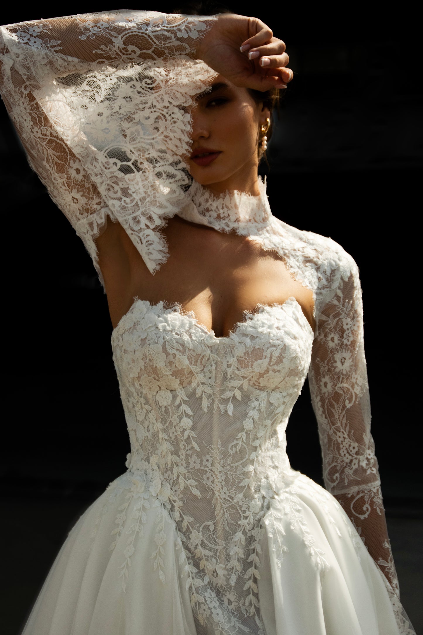 Bride wearing lace long-sleeve wedding dress with high illusion neckline, fitted corset bodice, and chapel train, featuring intricate lace cuffs and back detailing.