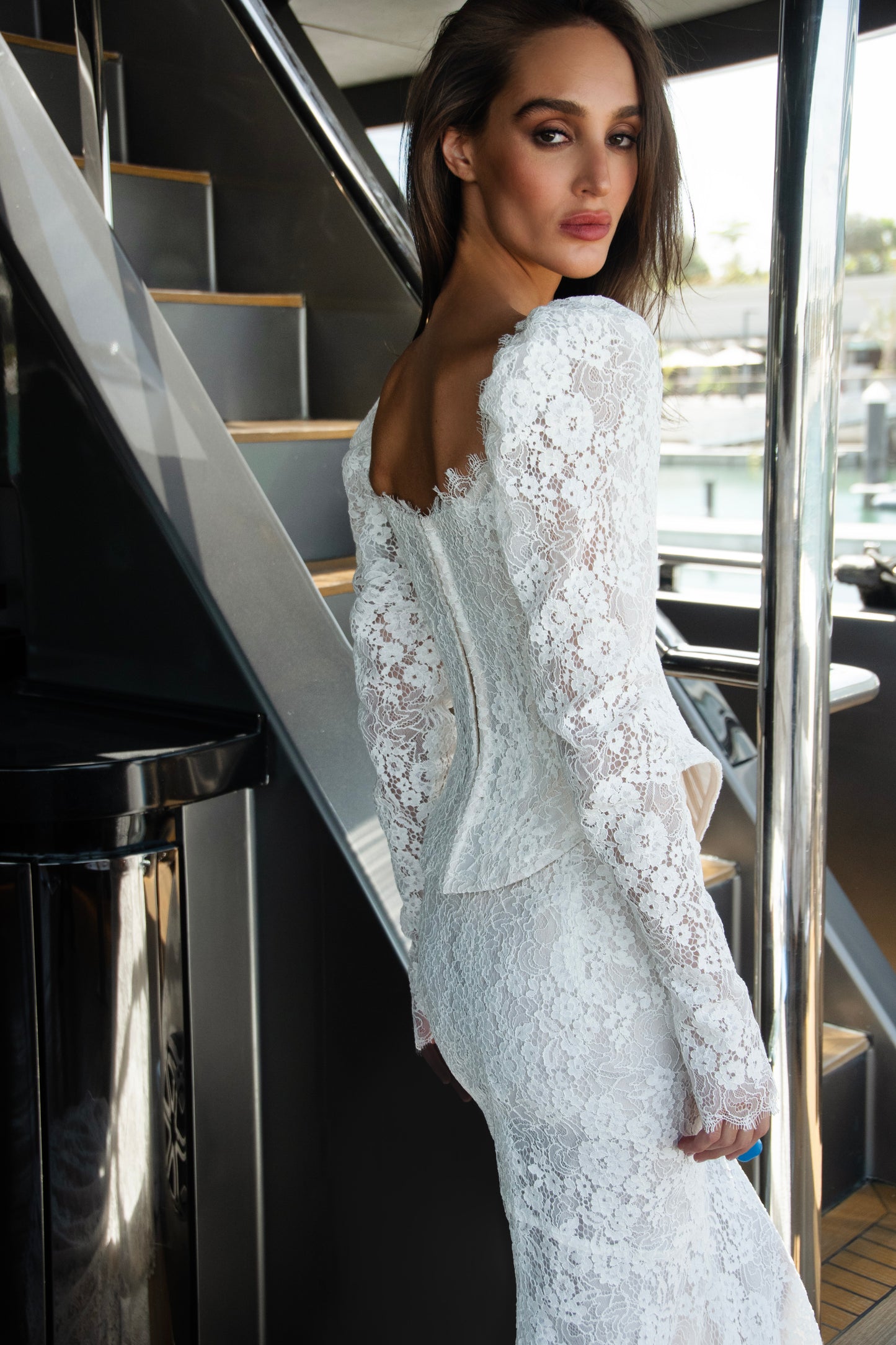 Long sleeve lace wedding dress with corset bodice and detachable 3D petal overskirt, featuring chapel-length train.