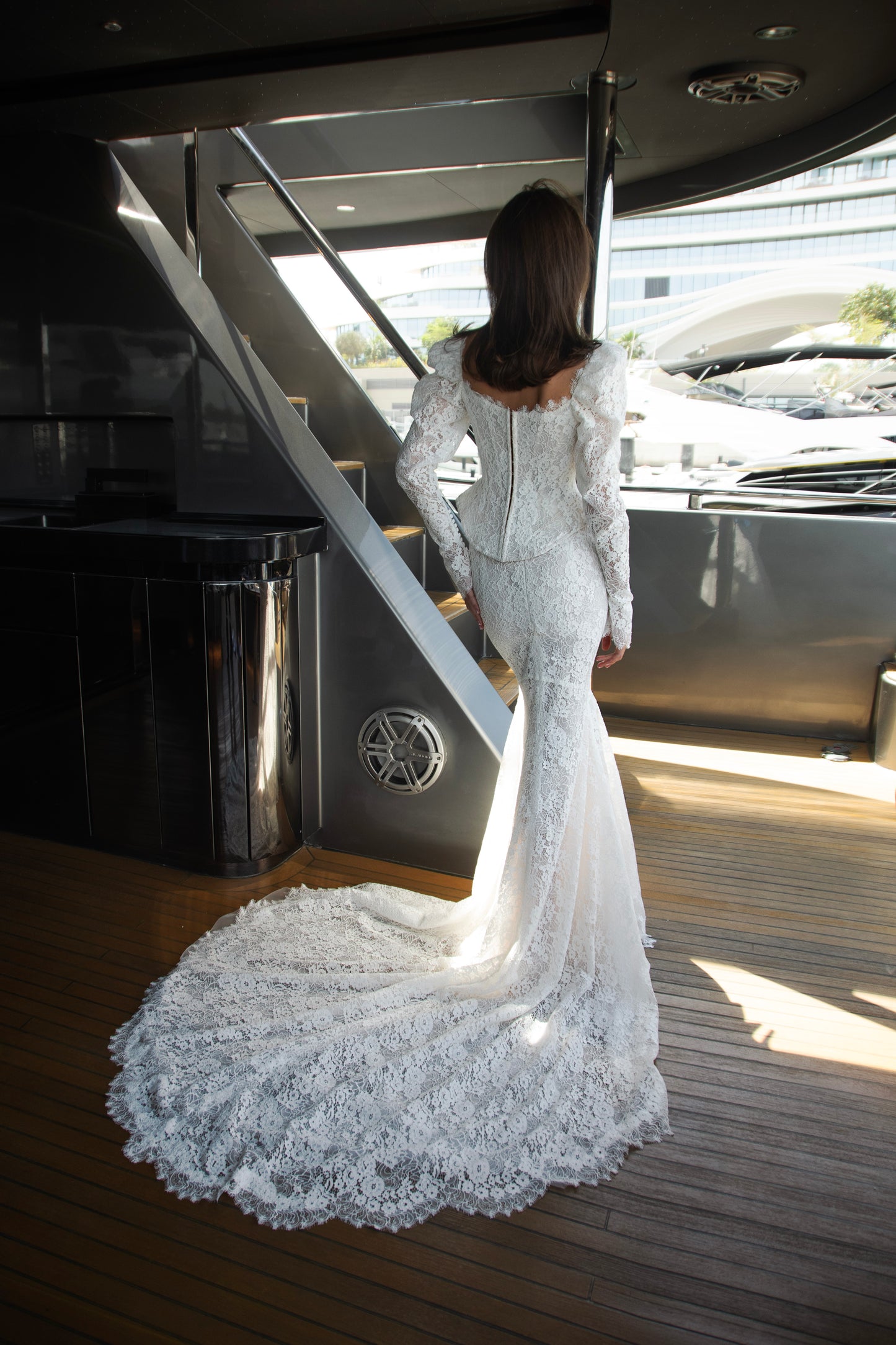 Long sleeve lace wedding dress with corset bodice and detachable 3D petal overskirt, featuring chapel-length train.
