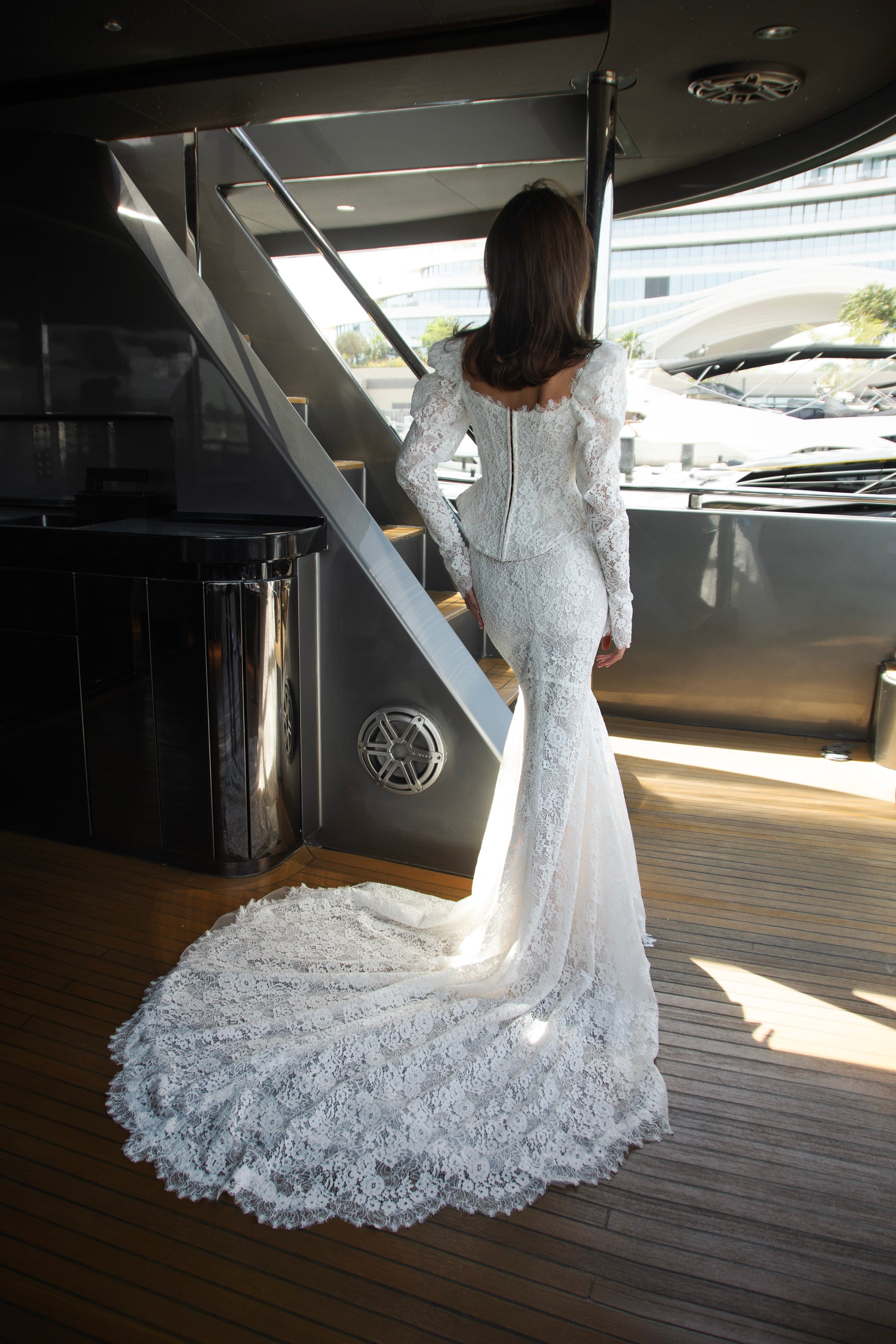 Long sleeve lace wedding dress with corset bodice and detachable 3D petal overskirt, featuring chapel-length train.