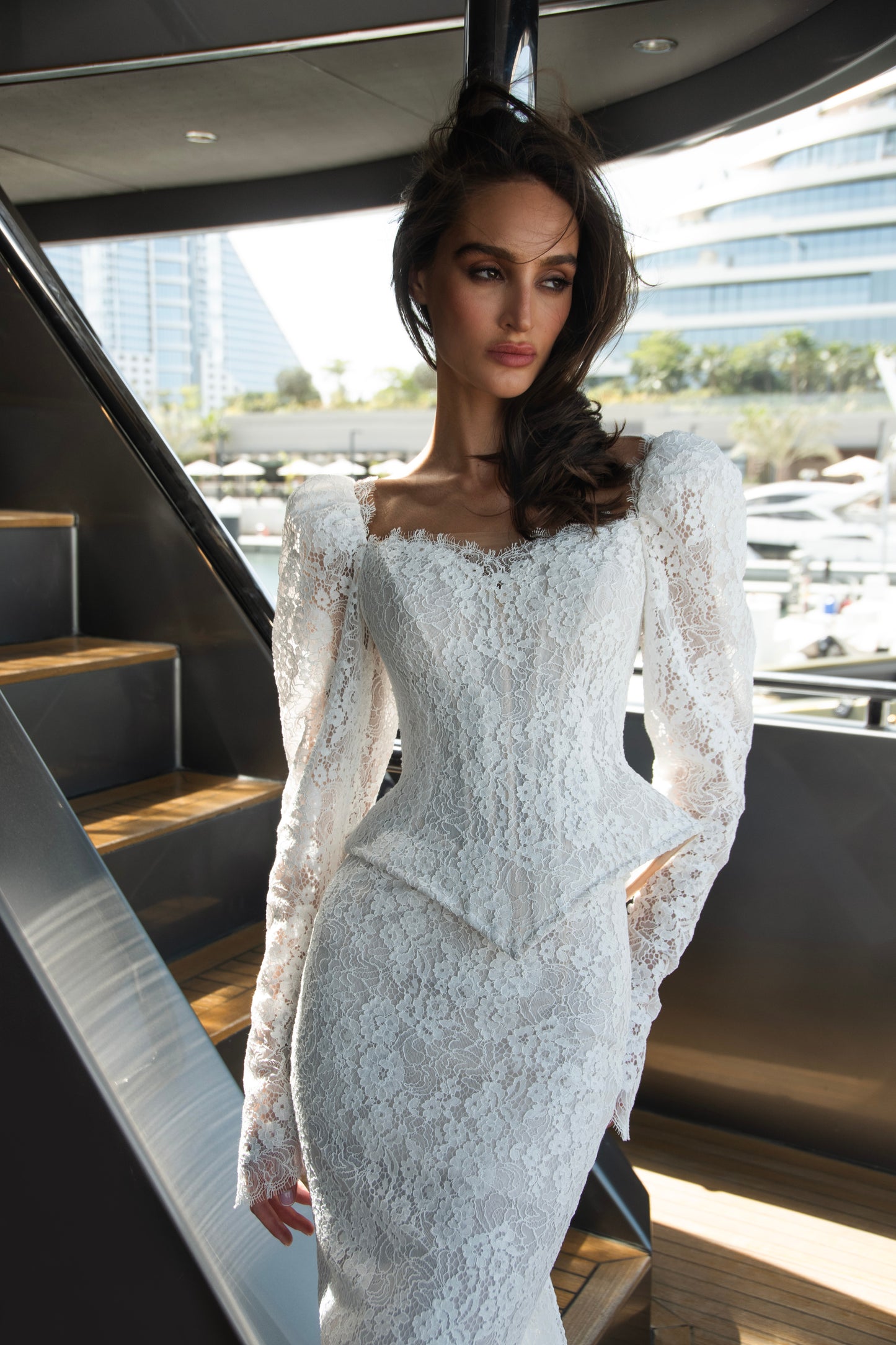 Long sleeve lace wedding dress with corset bodice and detachable 3D petal overskirt, featuring chapel-length train.