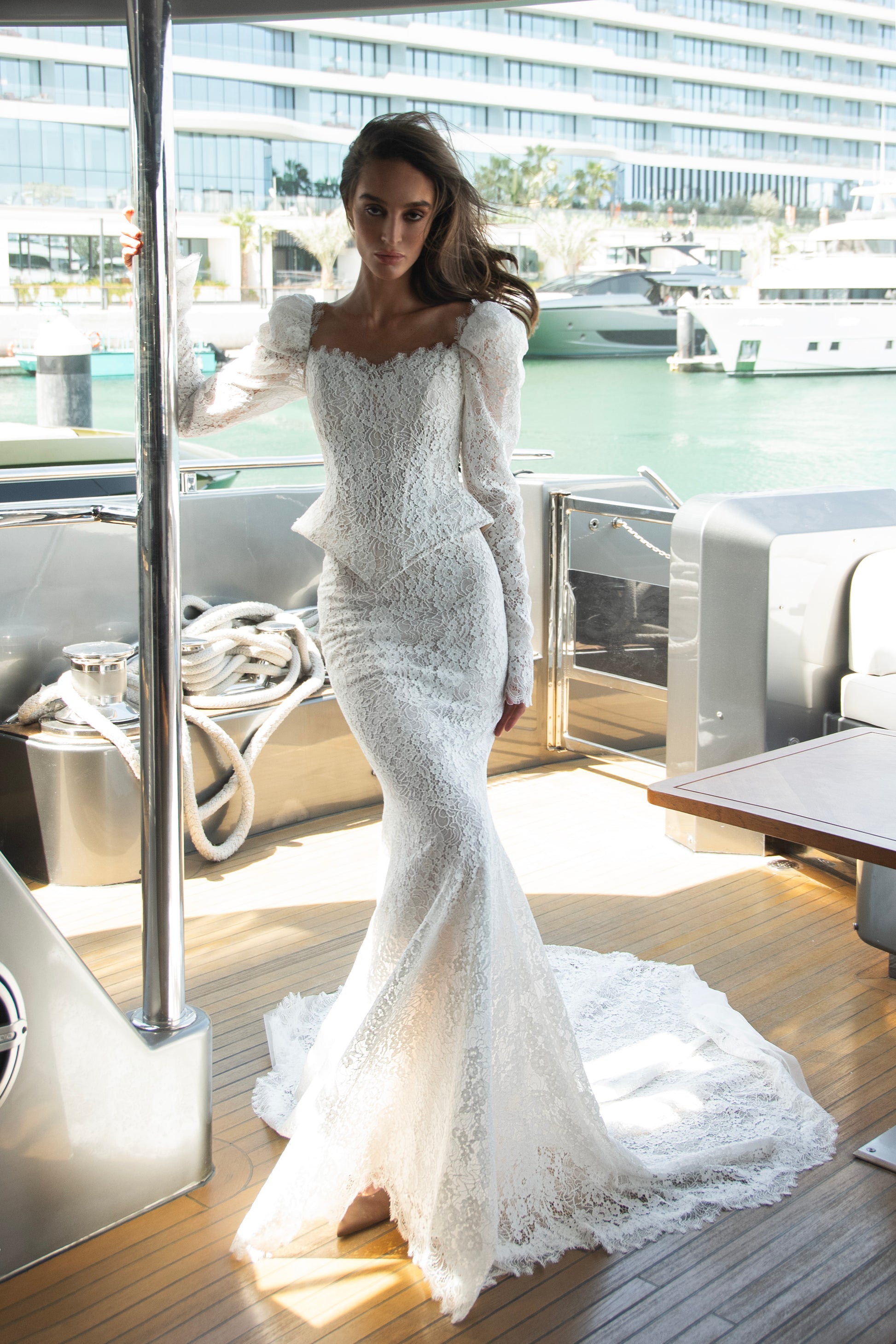 Long sleeve lace wedding dress with corset bodice and detachable 3D petal overskirt, featuring chapel-length train.