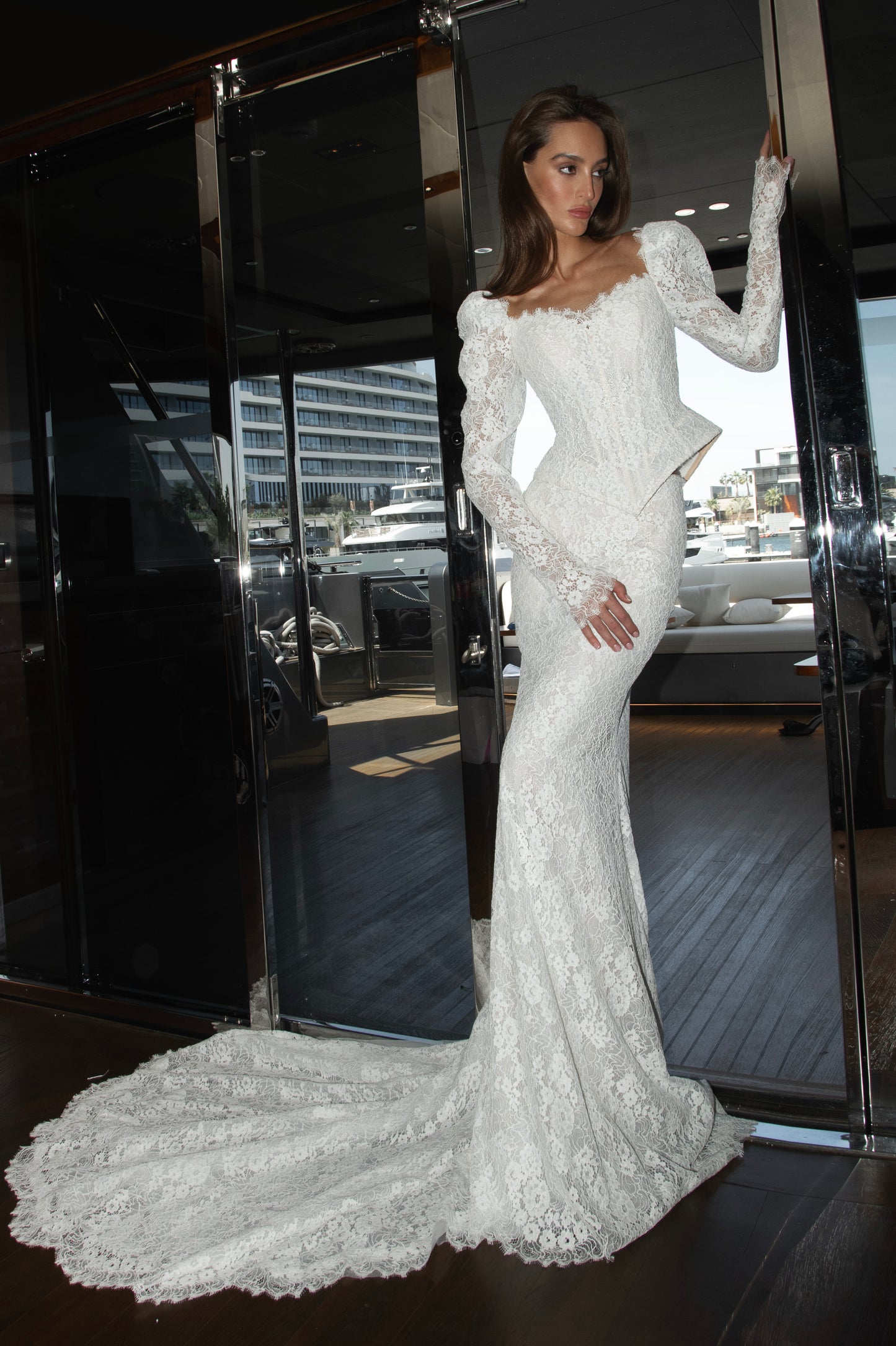 Long sleeve lace wedding dress with corset bodice and detachable 3D petal overskirt, featuring chapel-length train.