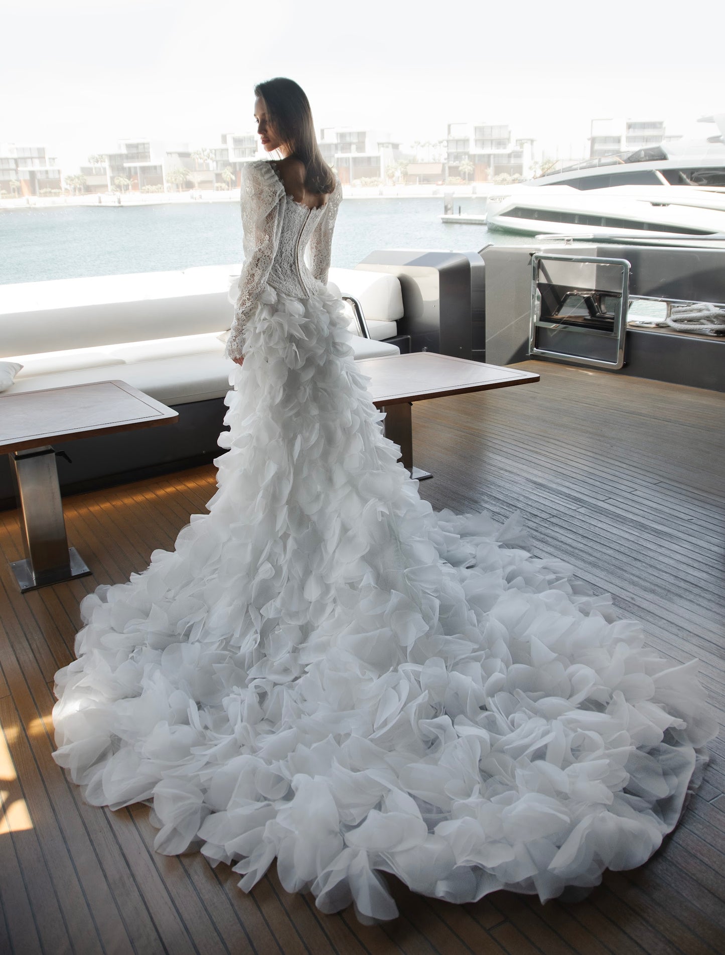 Long sleeve lace wedding dress with corset bodice and detachable 3D petal overskirt, featuring chapel-length train.