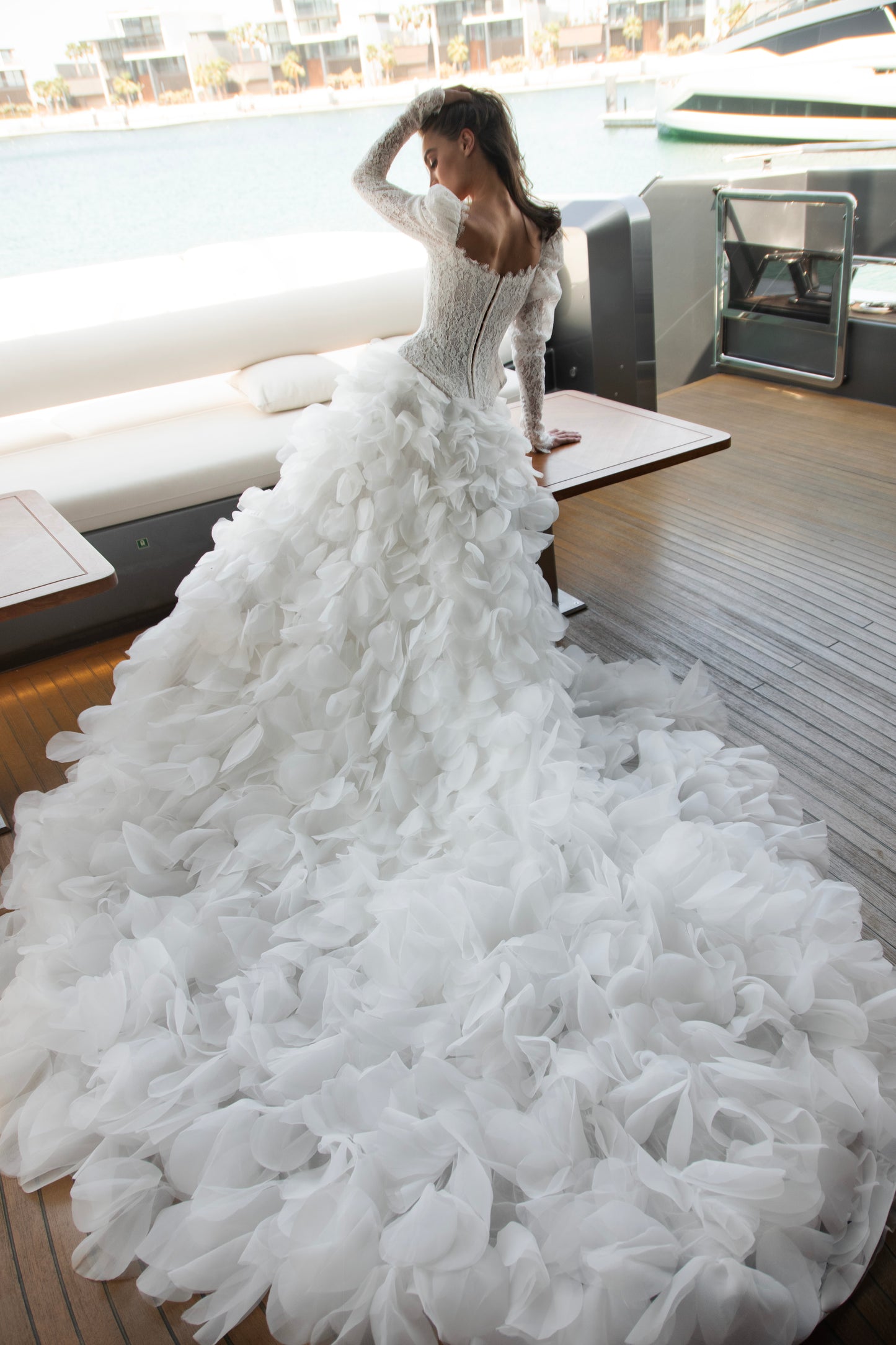 Long sleeve lace wedding dress with corset bodice and detachable 3D petal overskirt, featuring chapel-length train.