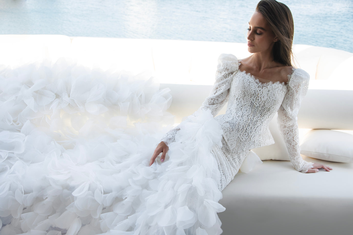 Long sleeve lace wedding dress with corset bodice and detachable 3D petal overskirt, featuring chapel-length train.