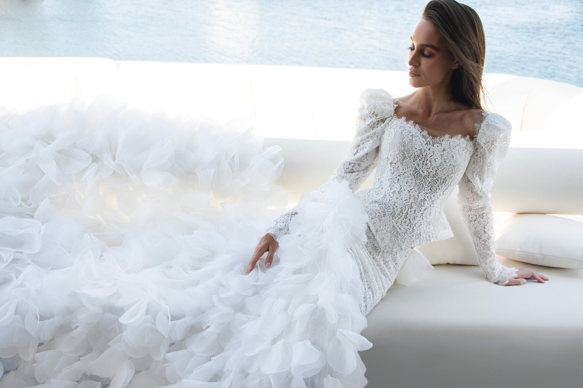 Long sleeve lace wedding dress with corset bodice and detachable 3D petal overskirt, featuring chapel-length train.