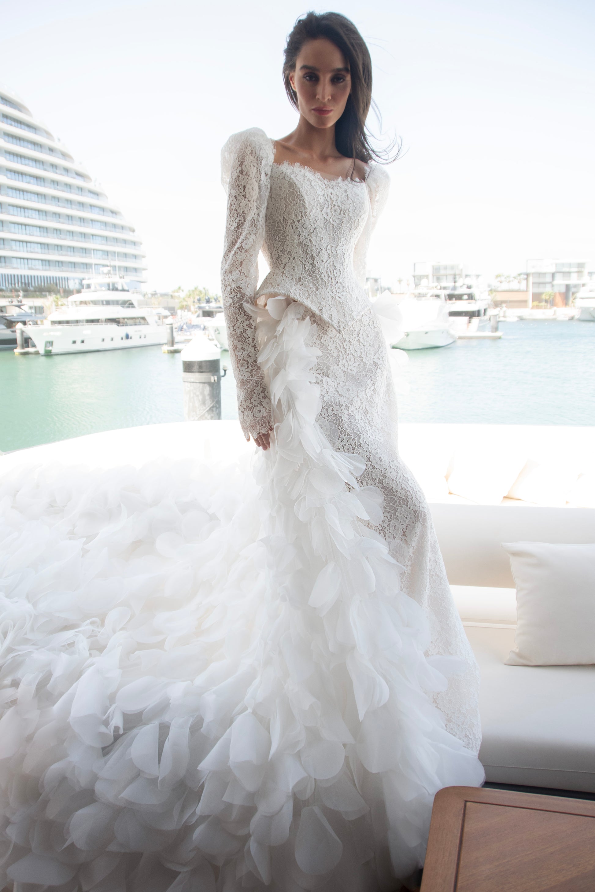 Long sleeve lace wedding dress with corset bodice and detachable 3D petal overskirt, featuring chapel-length train.