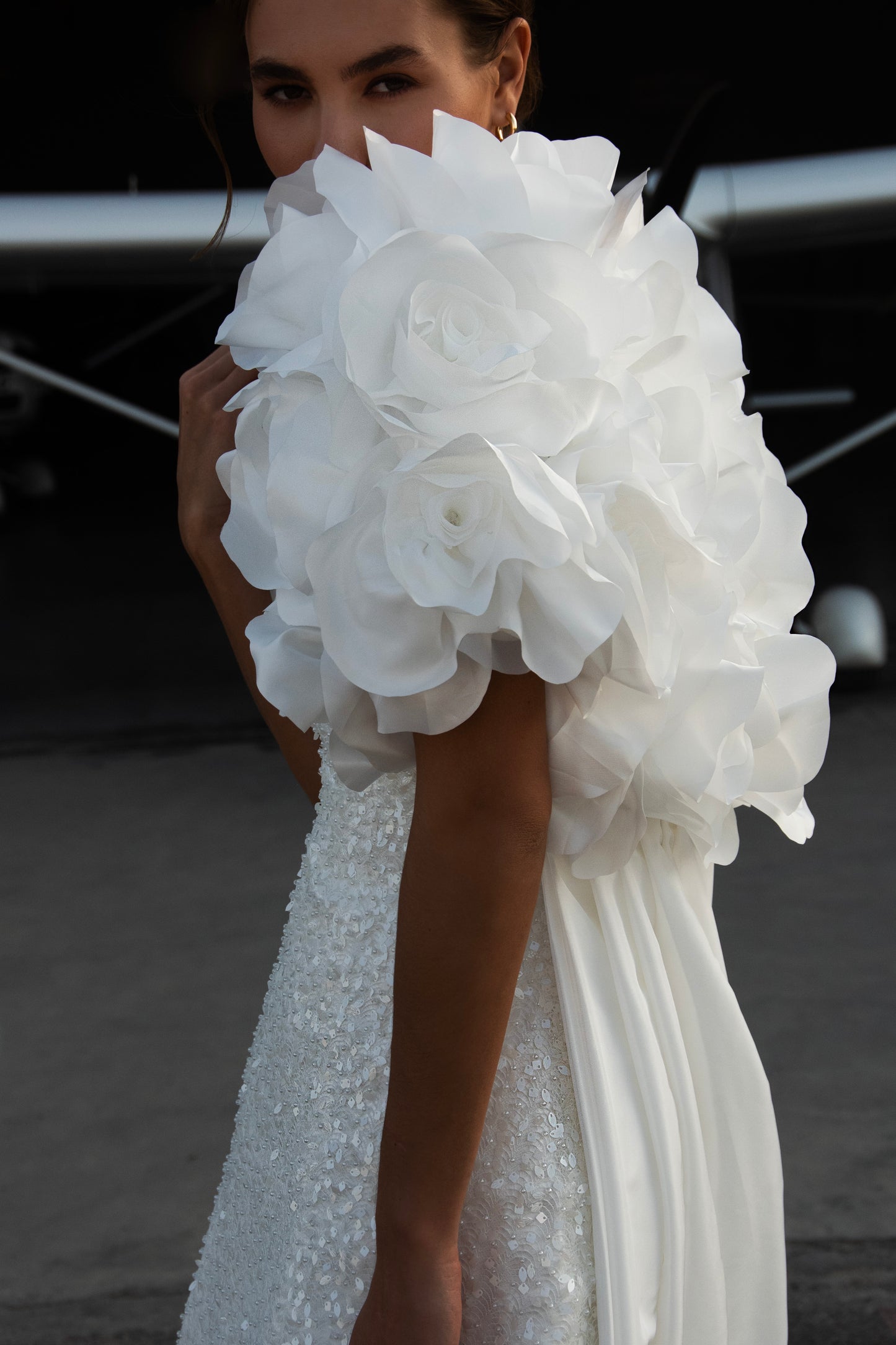 Bride wearing short beaded mini wedding dress with voluminous floral bolero and detachable satin train, photographed at sunset airfield.