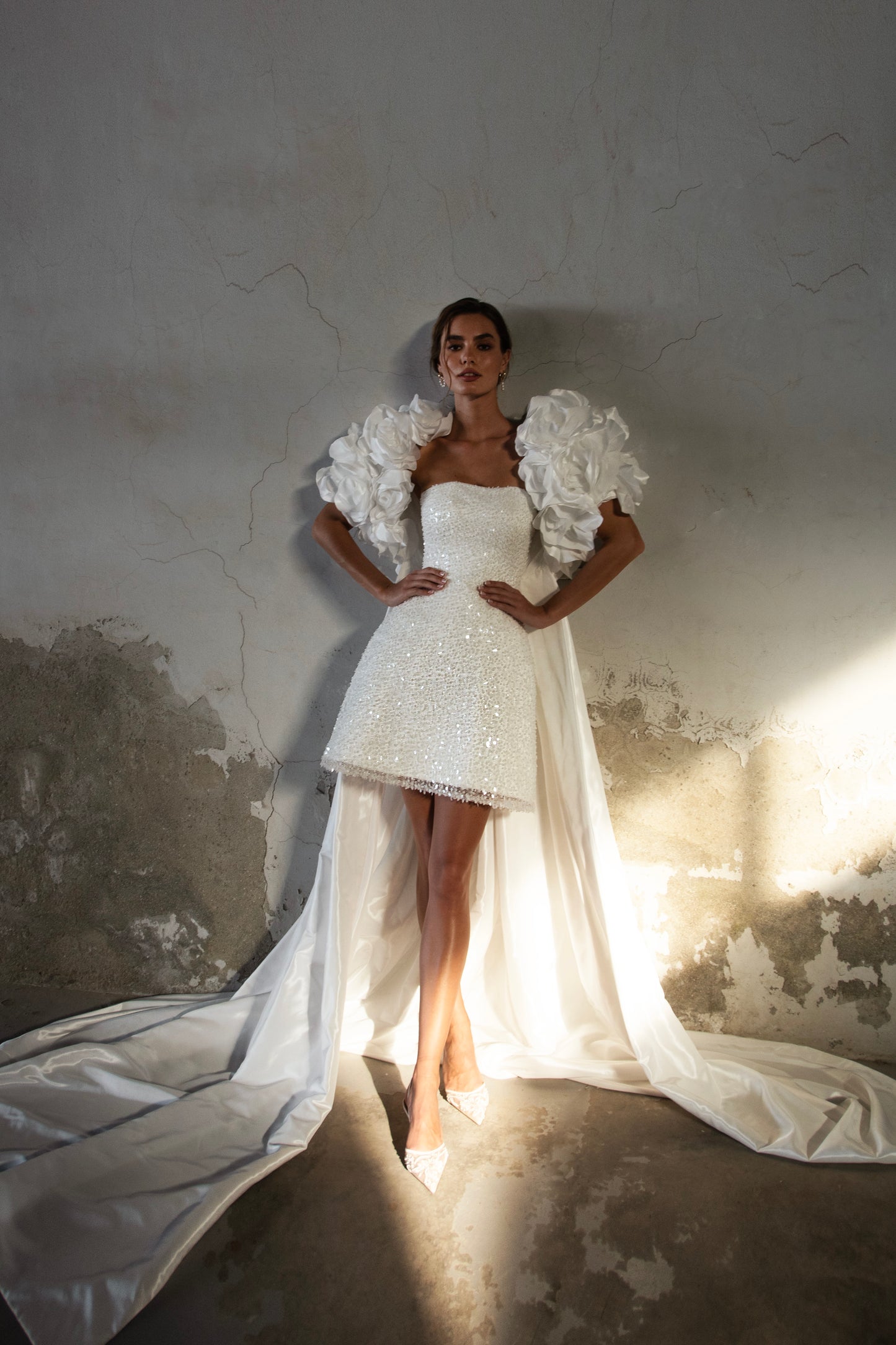 Bride wearing short beaded mini wedding dress with voluminous floral bolero and detachable satin train, photographed at sunset airfield.